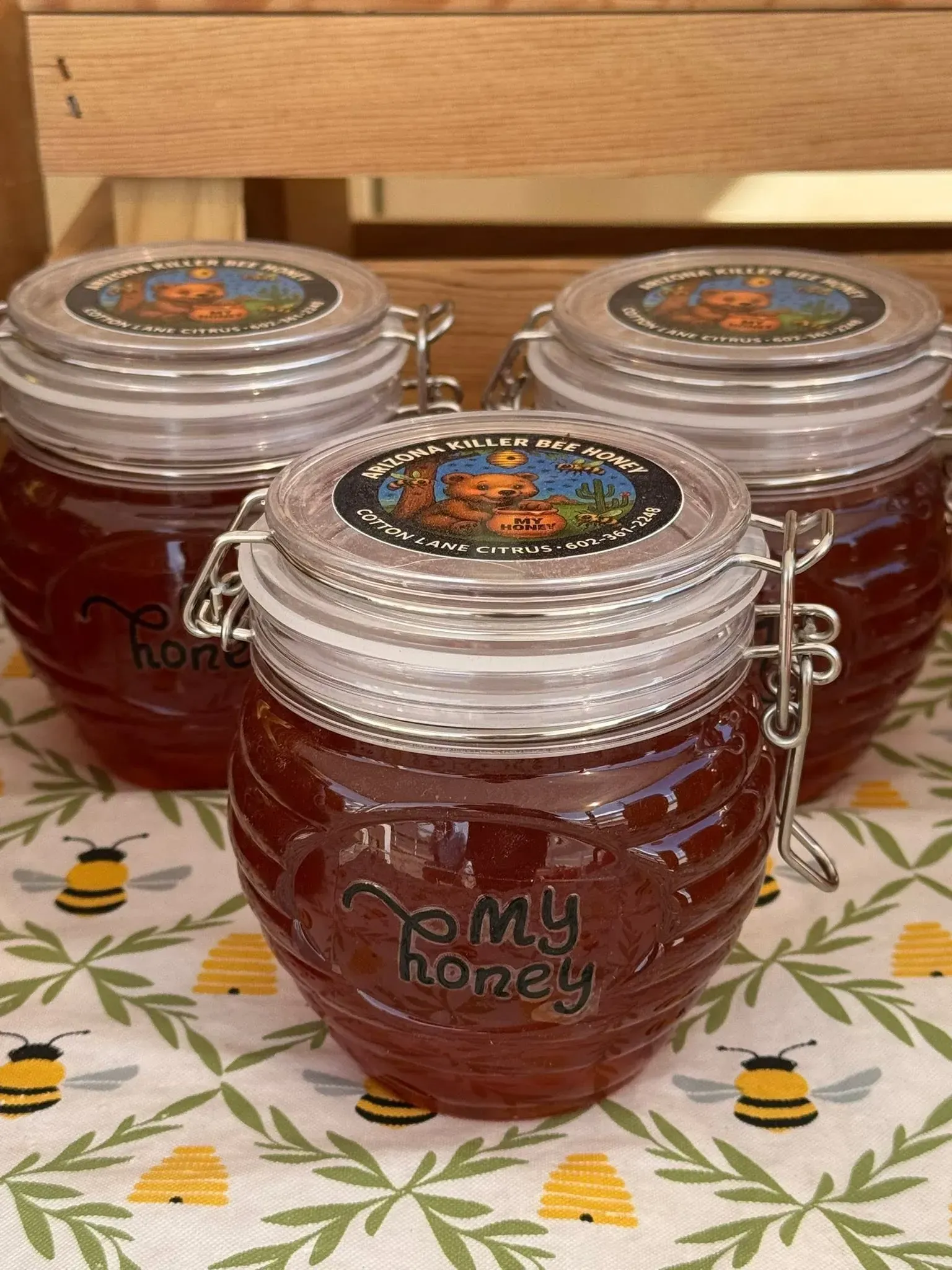 Three jars of amber honey with bee labels and clear clamp lids on a wooden table.