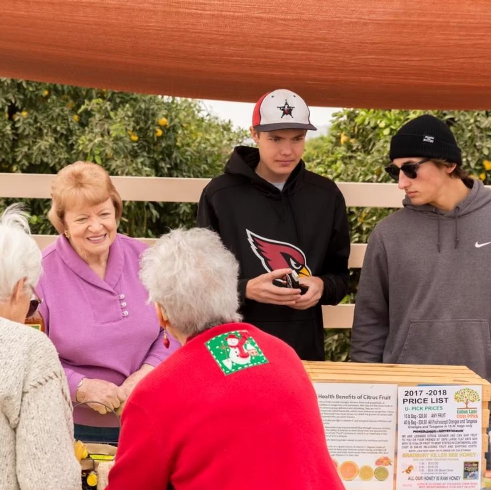People gathered at a food stand under an orange canopy, talking over a donation box.
