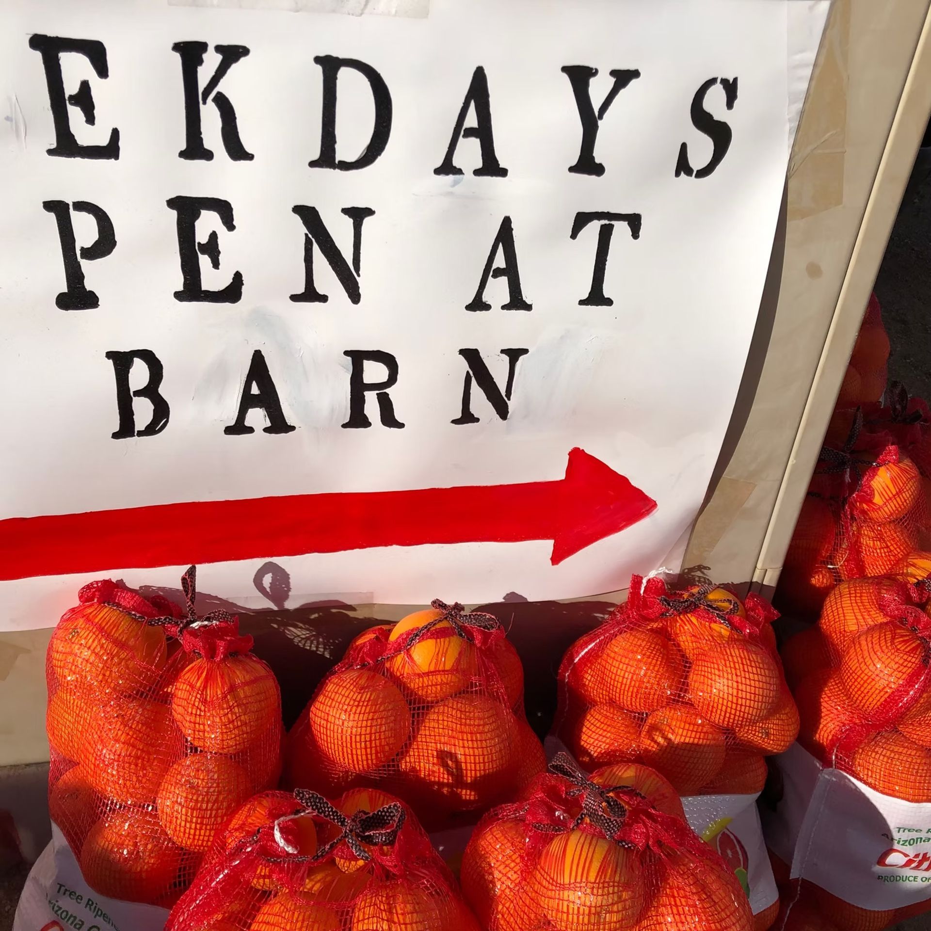 Market sign for “Ekdays Pen At Barn” with red arrow pointing to bags of oranges.