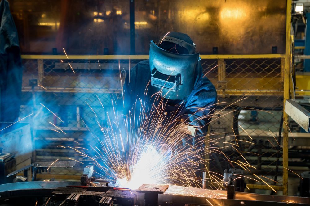 Welder in a blue helmet sparks bright metalwork in an industrial workshop