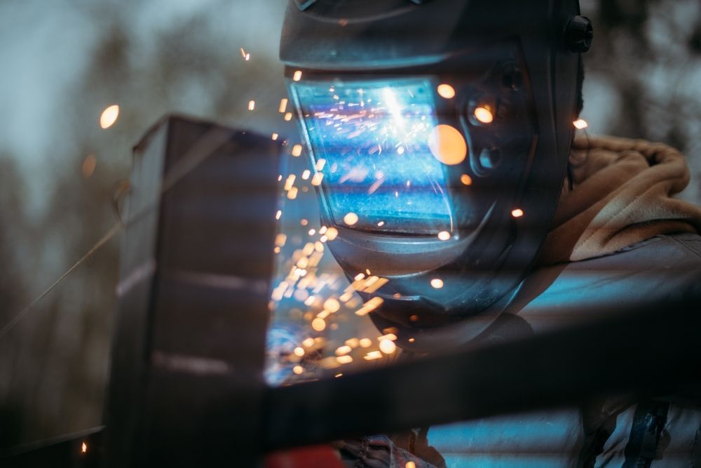 Welder in a helmet sparks flying as bright blue light glows in a dark workshop