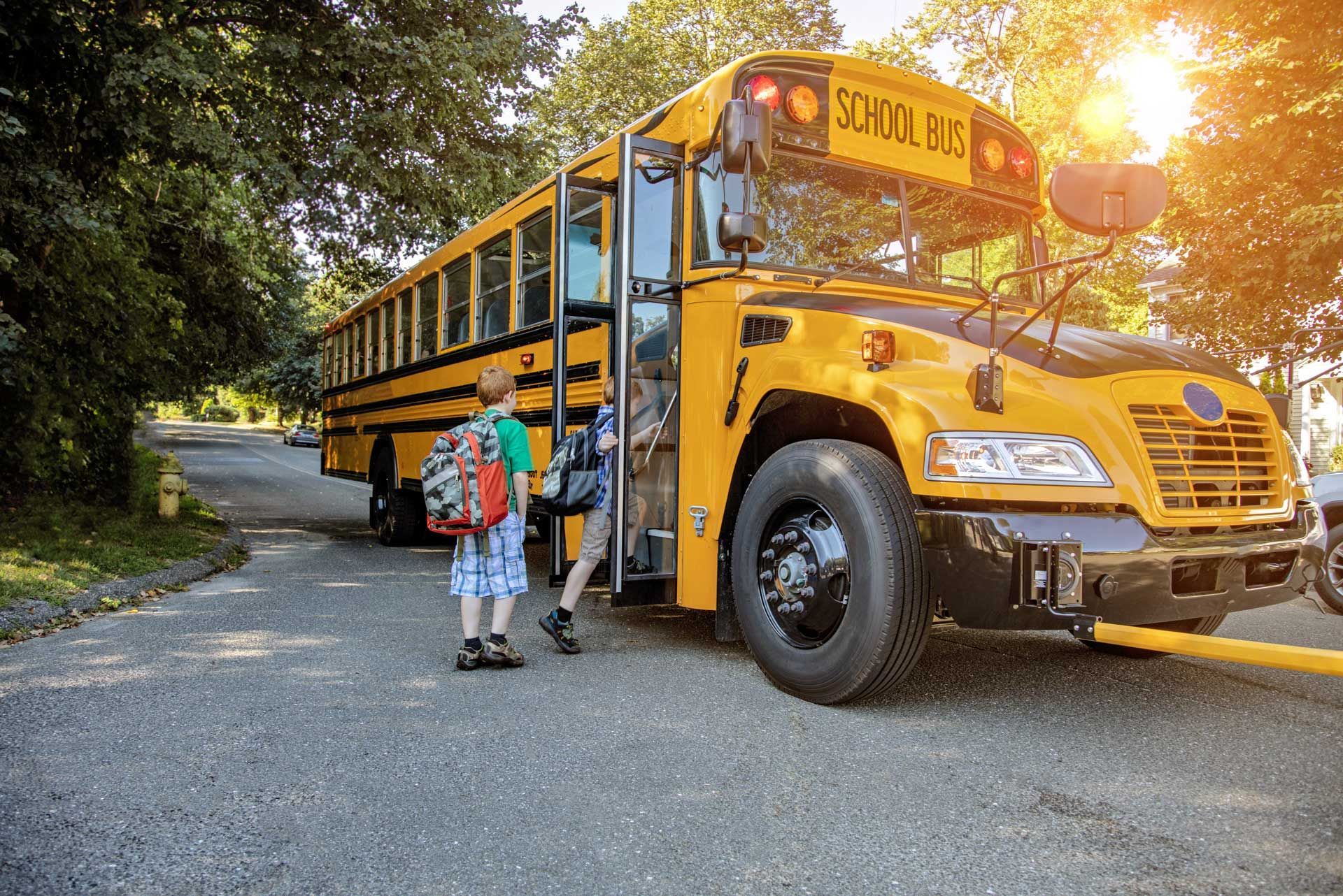 Two children are getting off a yellow school bus.