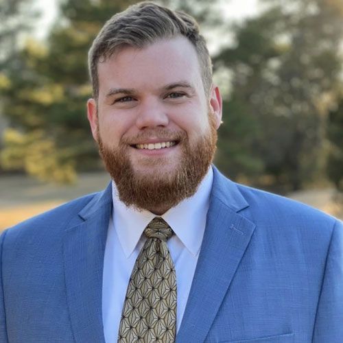 A man with a beard wearing a suit and tie is smiling for the camera.