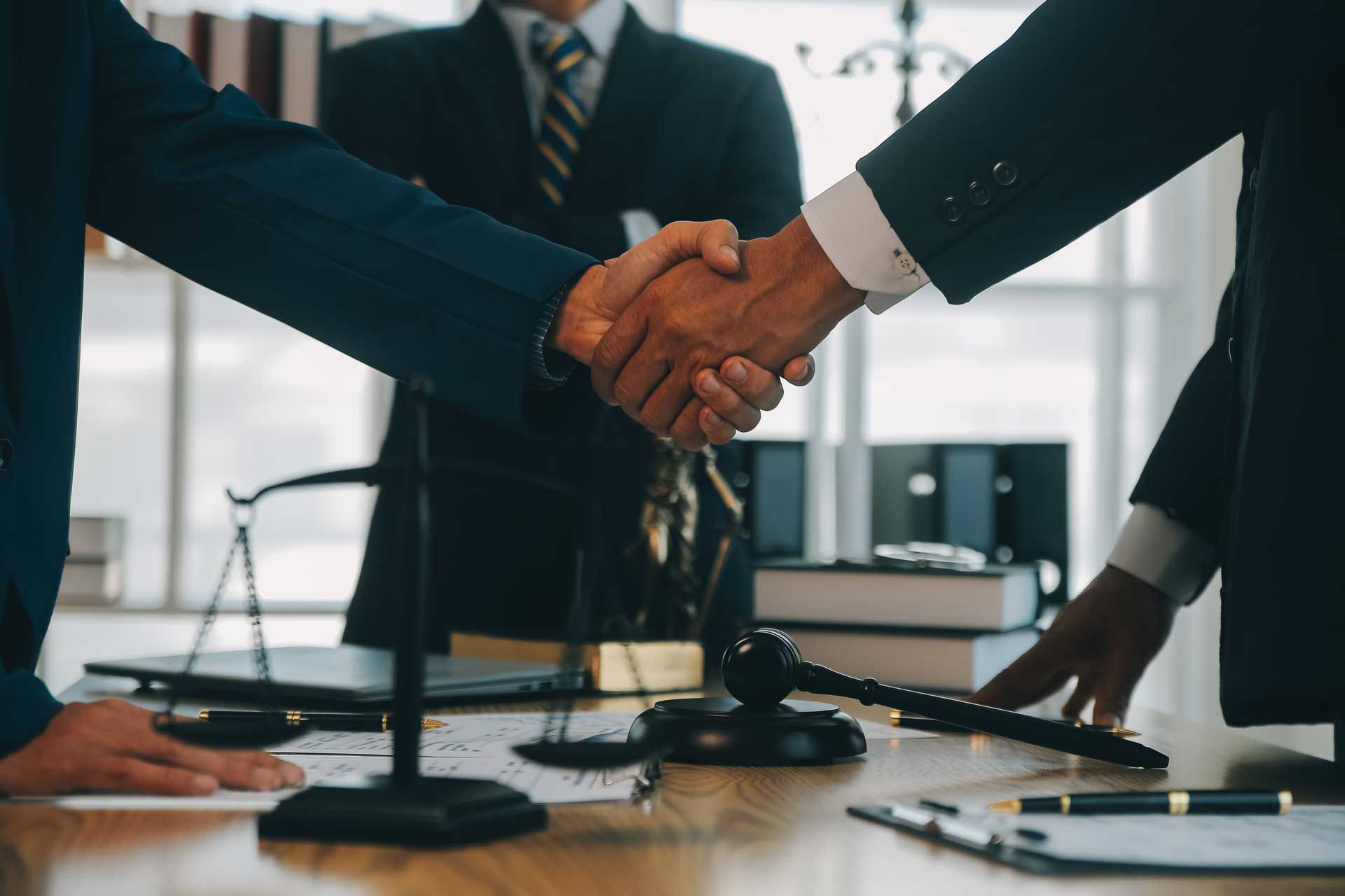 Two men are shaking hands in front of a judge 's gavel in a courtroom.