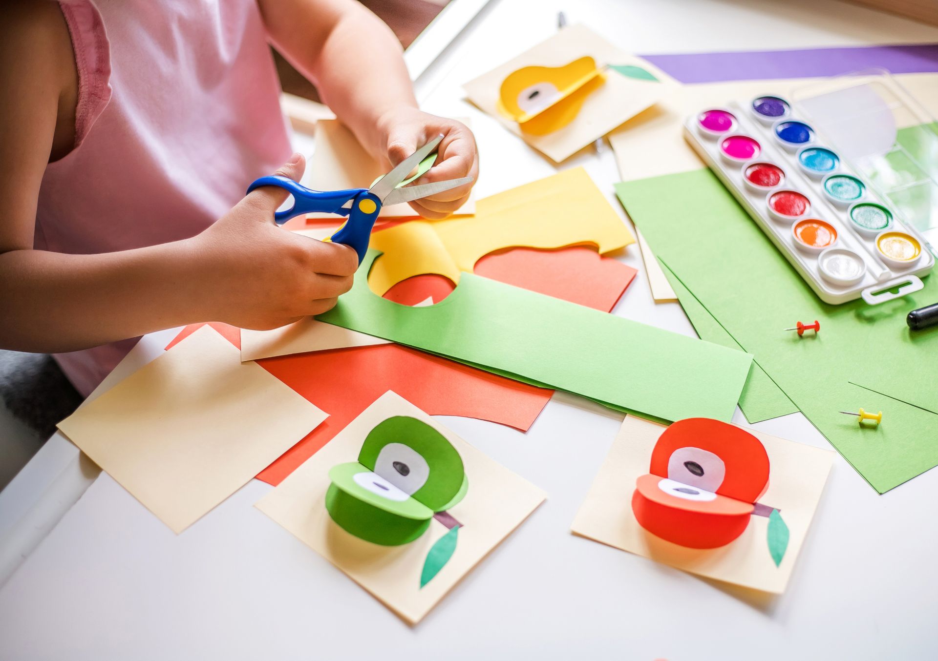 A little girl is cutting a piece of paper with scissors.