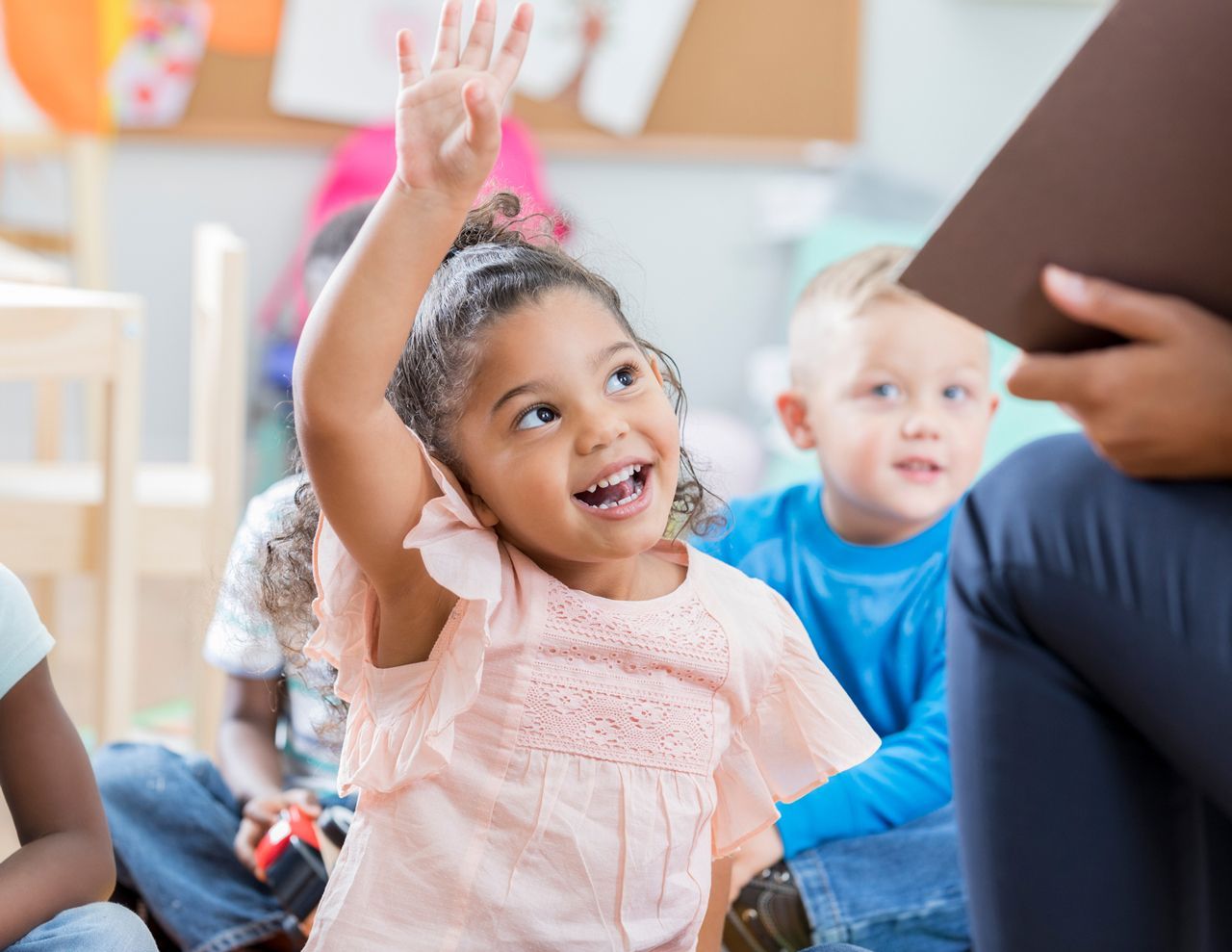 A little girl is raising her hand to answer a question in a classroom.