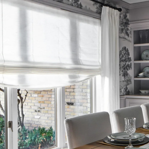 Bright dining room with a window seat, white curtains, built-in shelves, and a table set with dishes and glasses