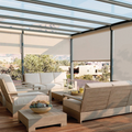Modern patio with beige outdoor sofa, chairs, coffee table, and a glass pergola overlooking a garden and buildings