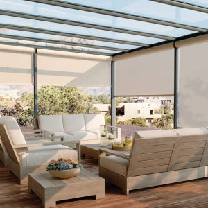 Modern patio with beige outdoor sofa, chairs, coffee table, and a glass pergola overlooking a garden and buildings
