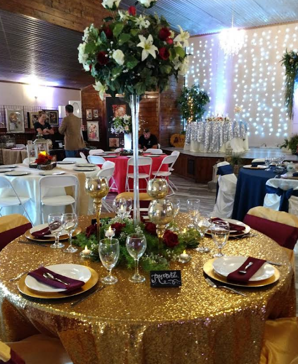 Reception table with gold sequin tablecloth, floral centerpiece, and place settings. Other tables visible.