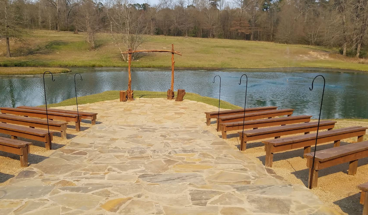 Outdoor wedding ceremony space with benches facing a pond and wooden arch.