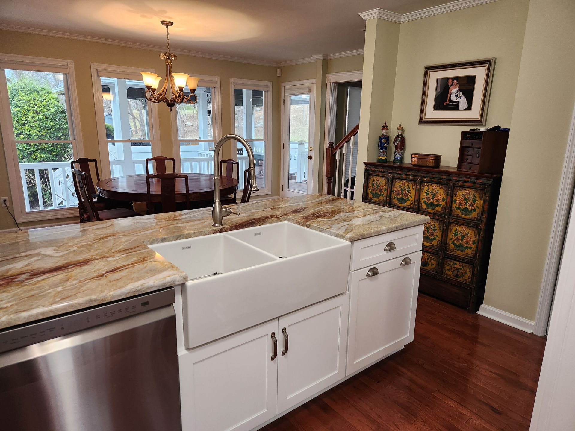Kitchen with white cabinets, granite countertop, farmhouse sink, stainless steel dishwasher, and a dining area.