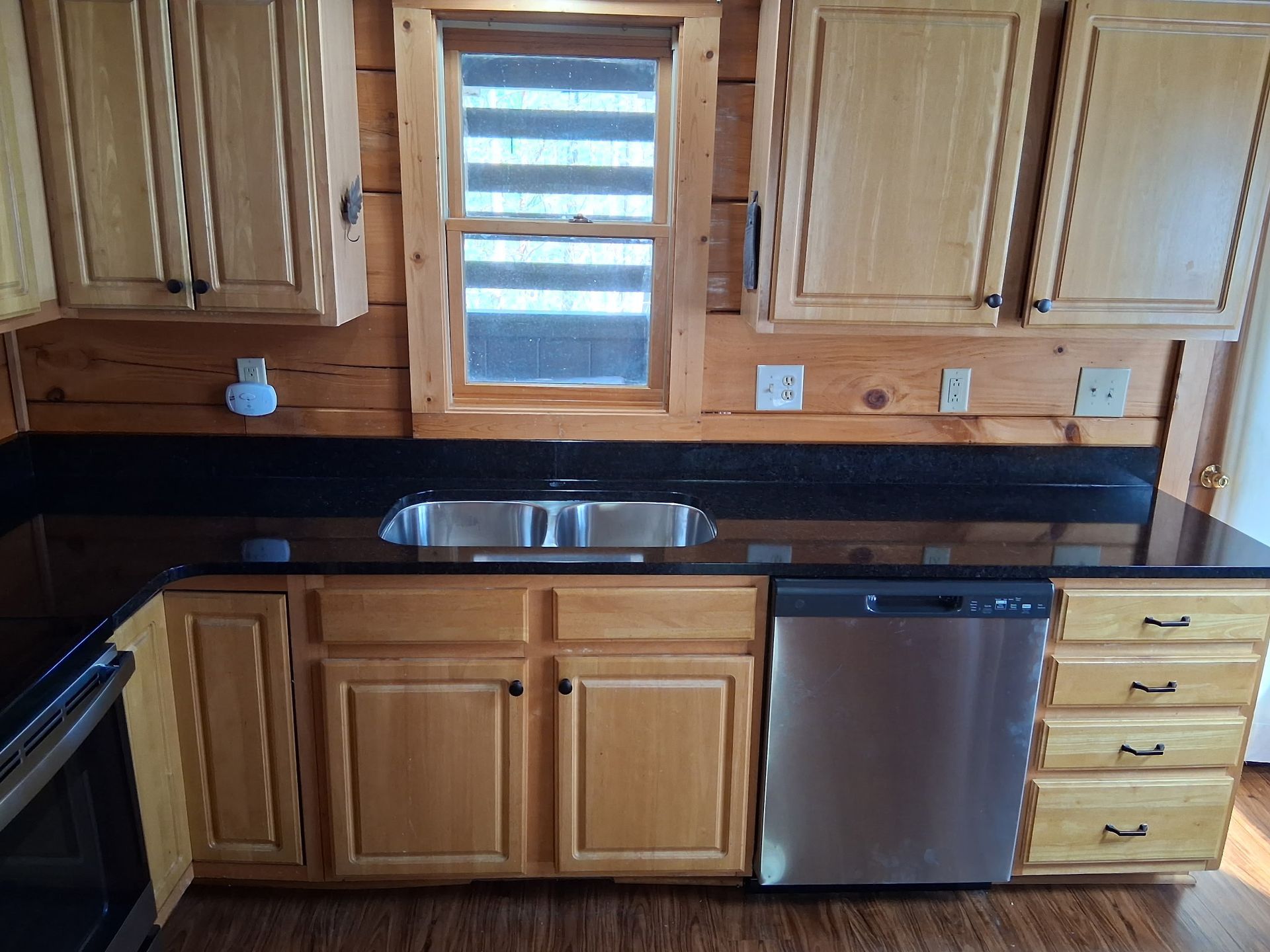 Kitchen with light wood cabinets, dark countertop, stainless steel appliances, and a window.