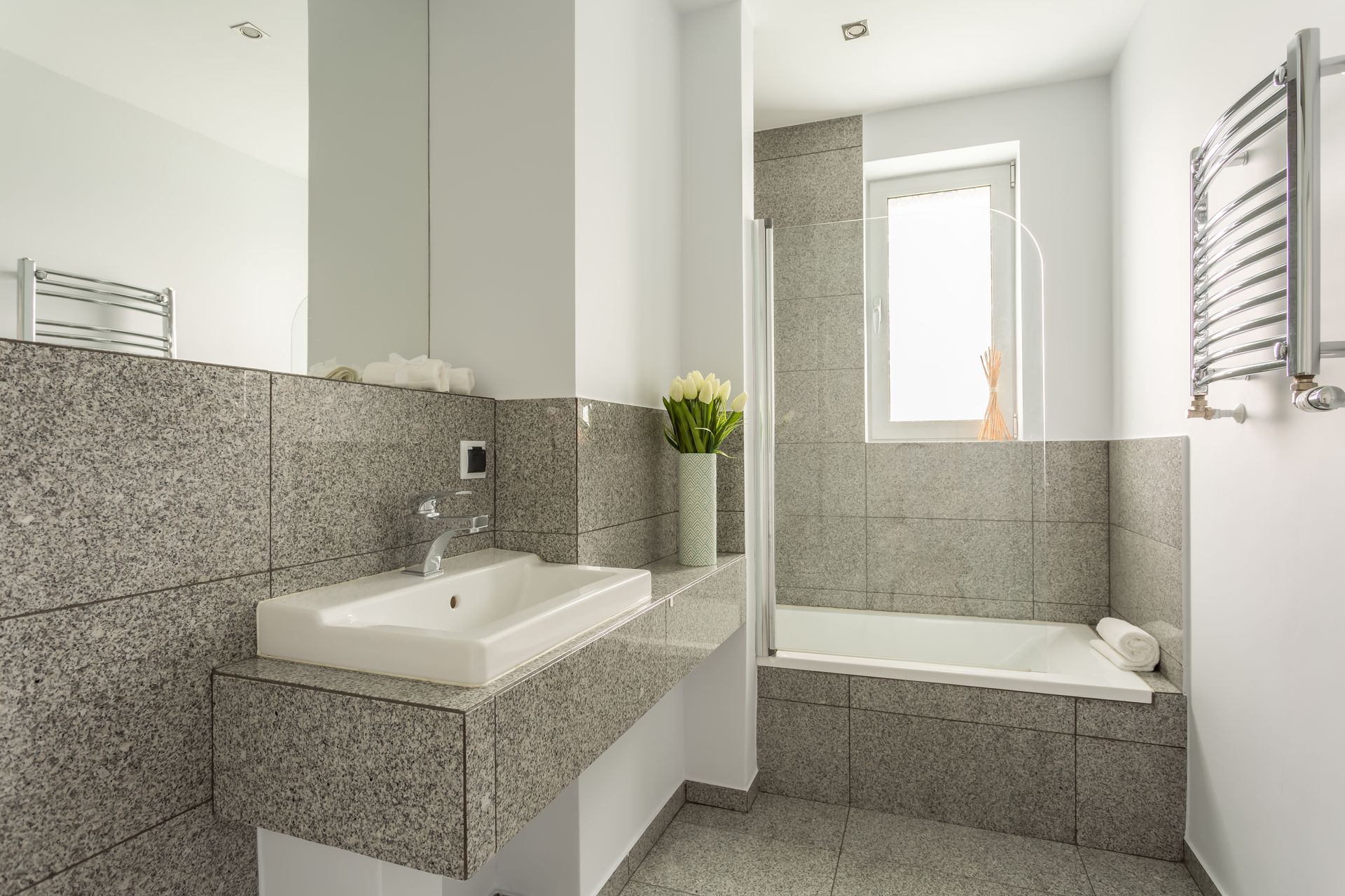 Modern bathroom featuring granite tile surfaces, a vanity sink, and a built-in bathtub.