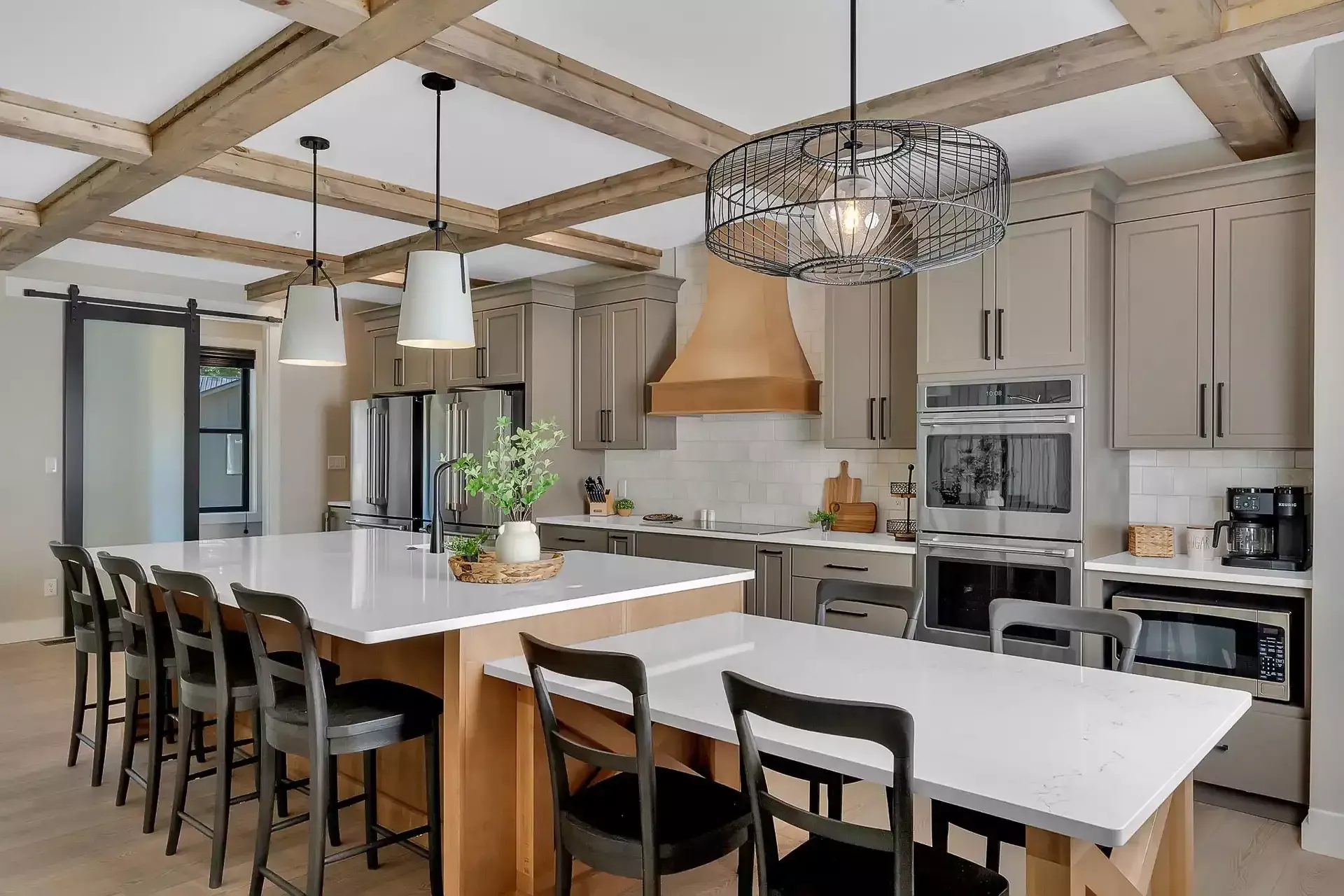 Modern kitchen with white island, black stools, wood beams, and stainless steel appliances