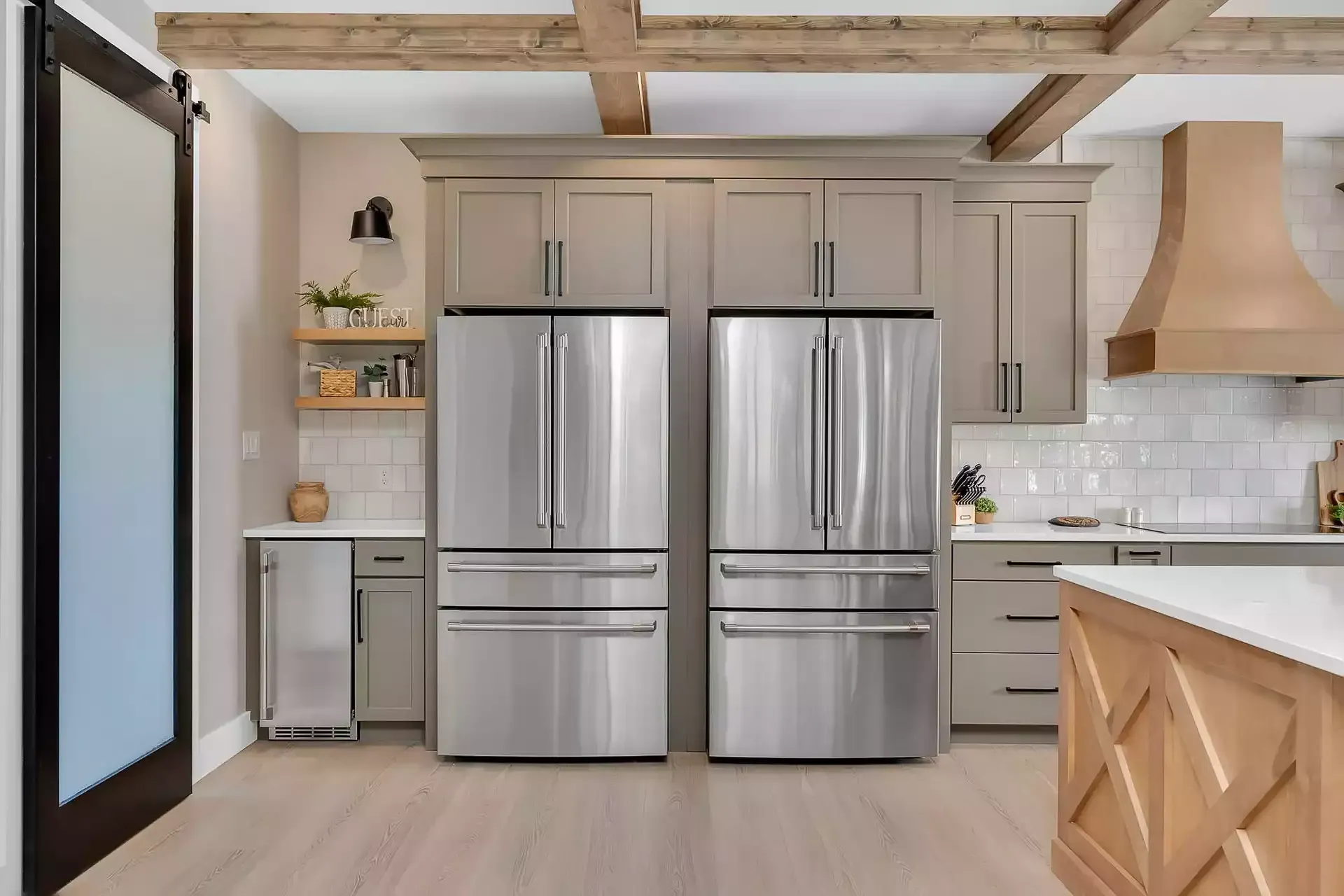 Kitchen with stainless steel refrigerators, wood cabinetry, and a light wooden floor.