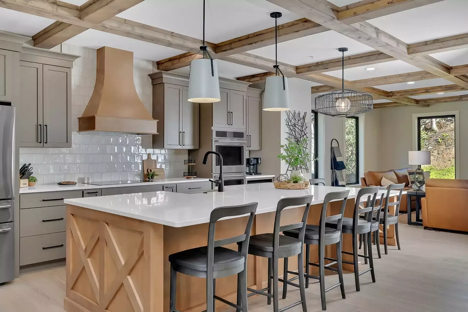 Modern kitchen with wood beams, large island, pendant lights, and dining area by windows