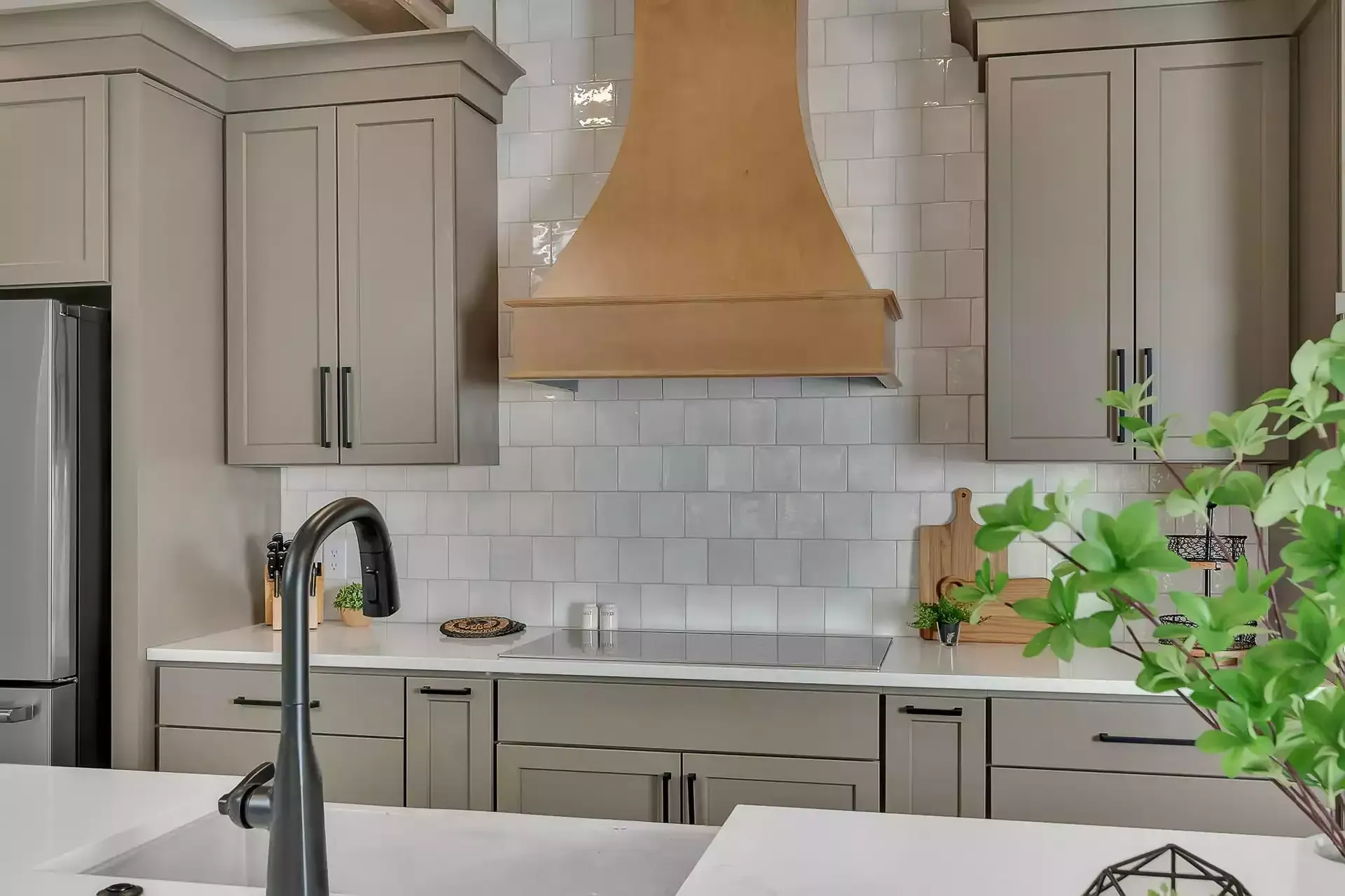 Modern kitchen with gray cabinets, wooden range hood, and white backsplash.