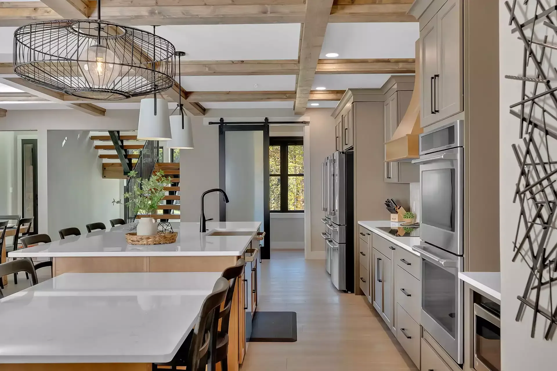 Modern kitchen with white island, black stools, wood beams, and stainless steel appliances