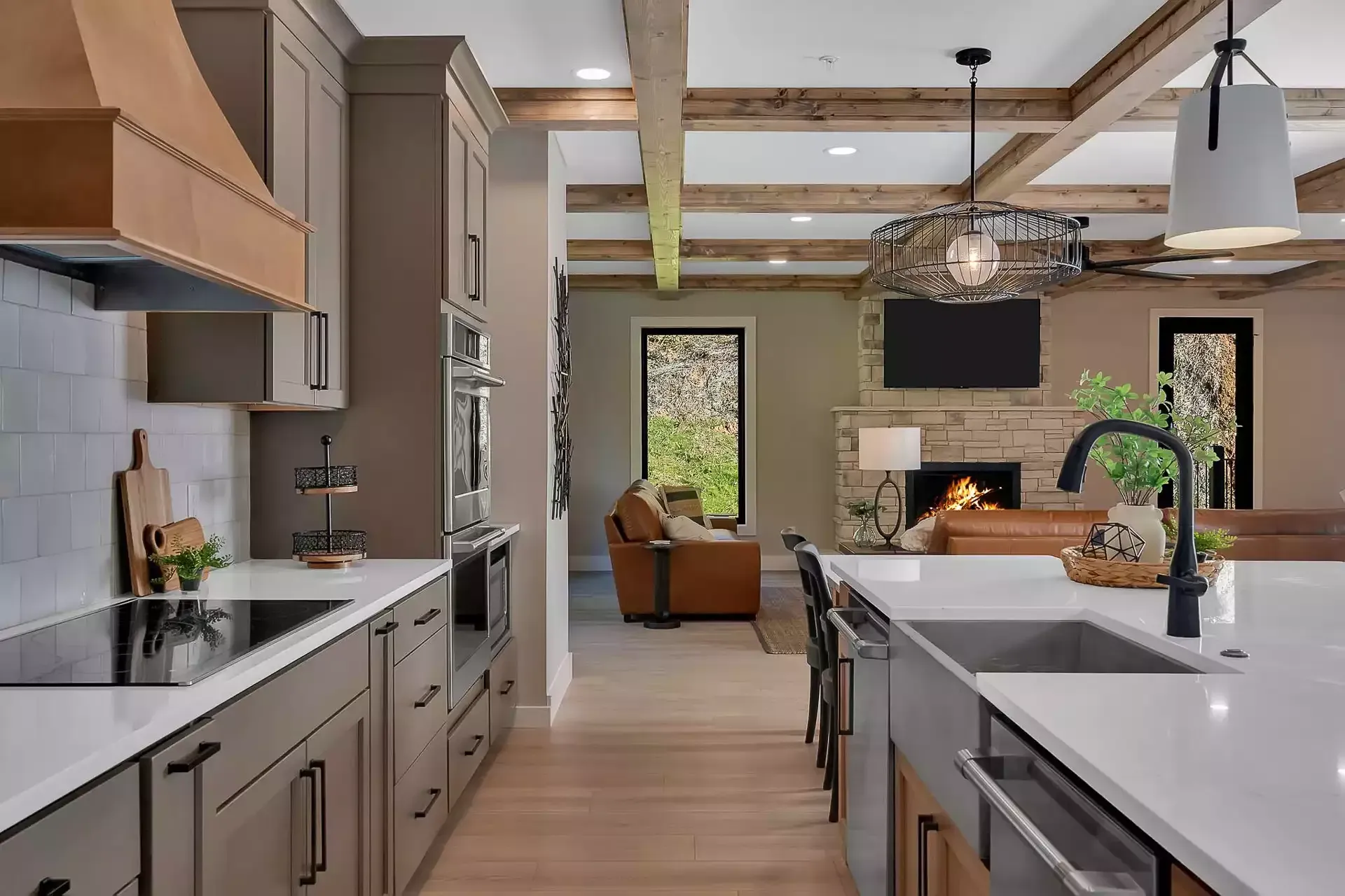 Modern kitchen with gray cabinets, white island counters, pendant lights, and a view into a bright living area