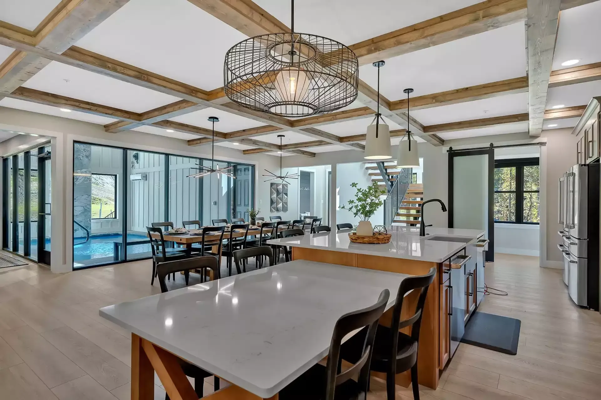 Bright modern kitchen and dining area with island, wood beams, chandelier, and pool view through glass doors