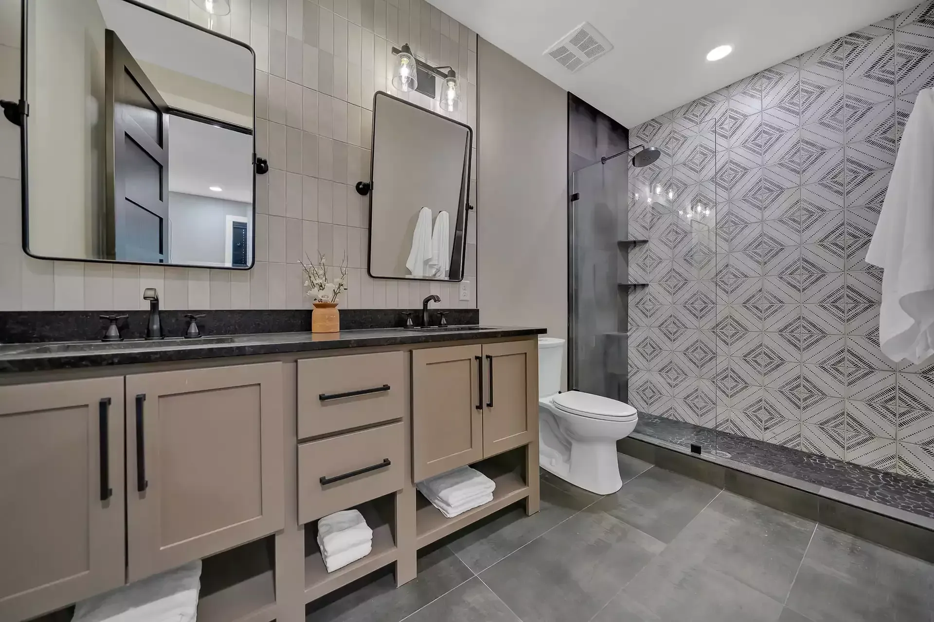 Bathroom with double vanity, two mirrors, tiled walls, and a walk-in shower.