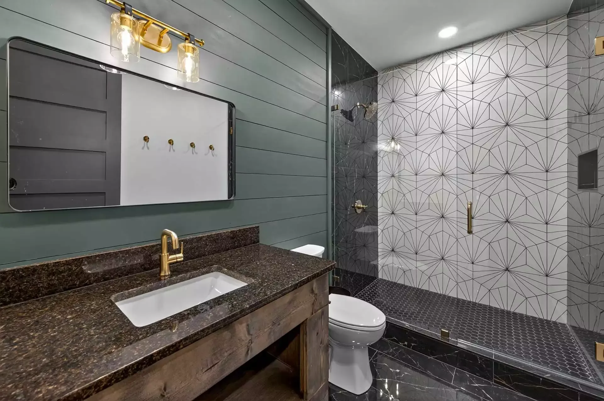 Modern bathroom with granite vanity, gold faucet, mirror, toilet, and tiled shower stall