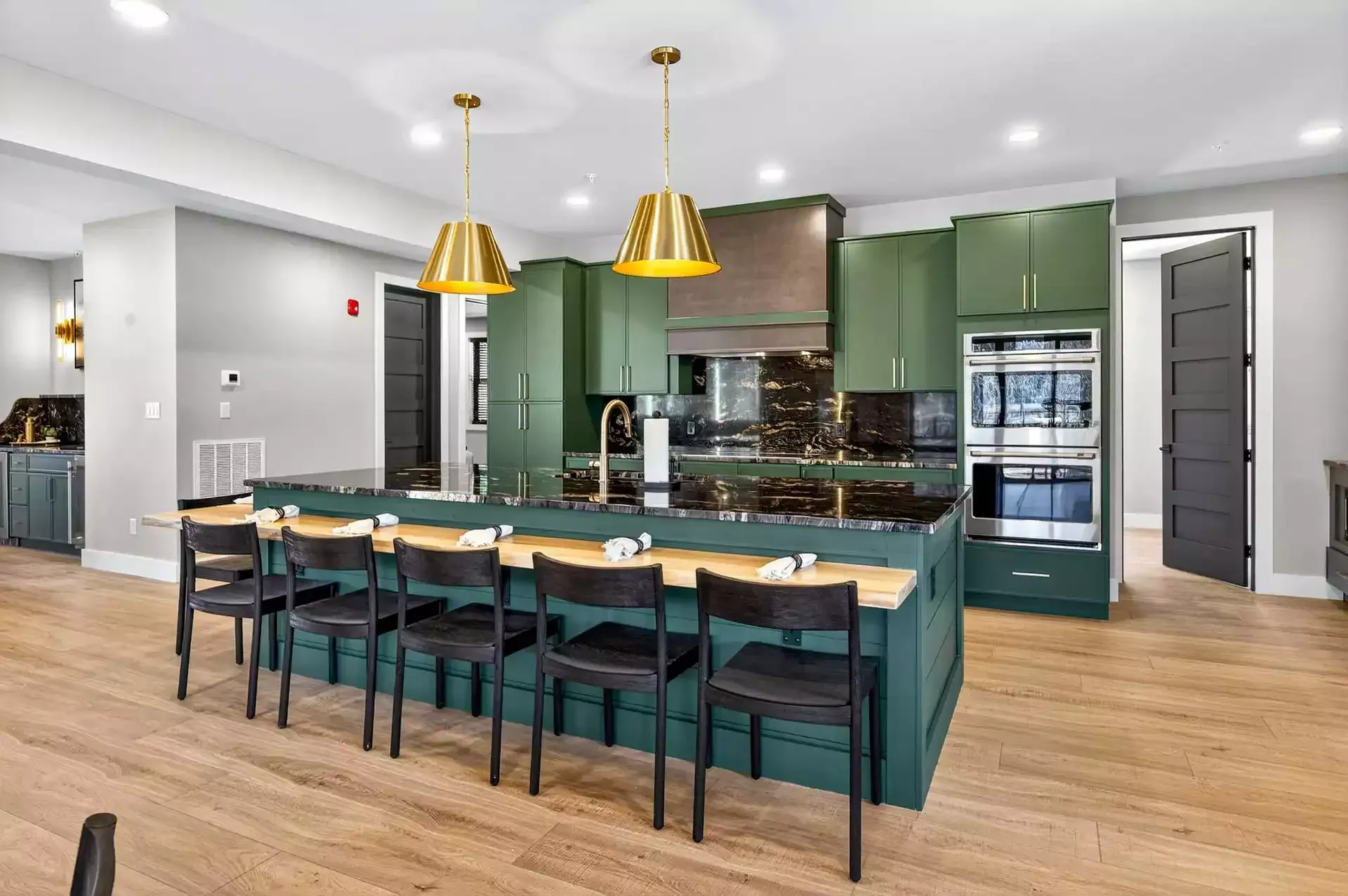Modern kitchen with green cabinets, marble island, teal chairs, and gold pendant lights