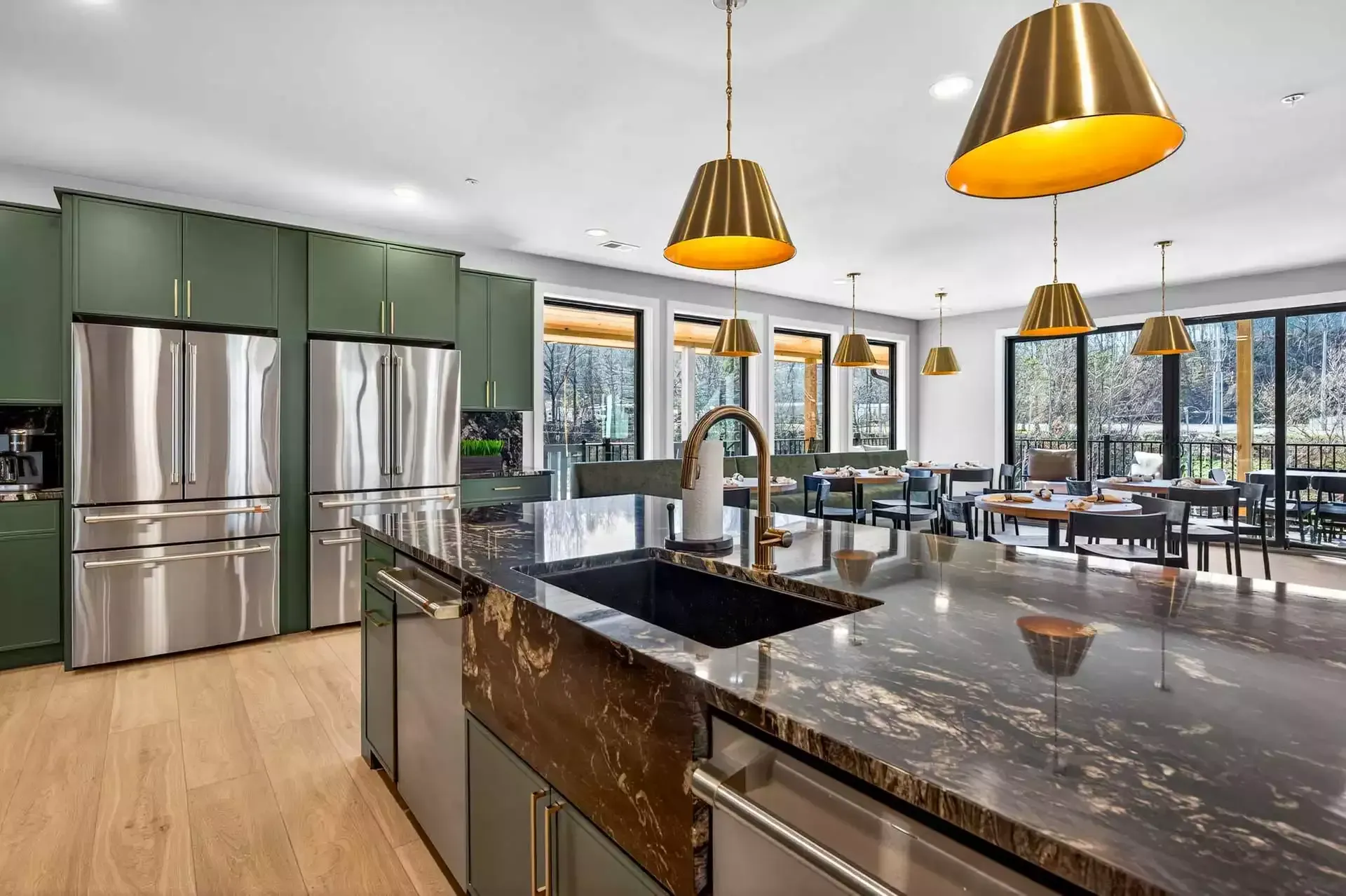 Modern kitchen with stainless steel appliances, green cabinets, island, and pendant lights overlooking a dining area