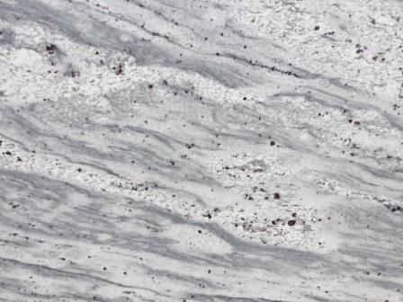 White and gray granite surface with wavy patterns and dark speckles.