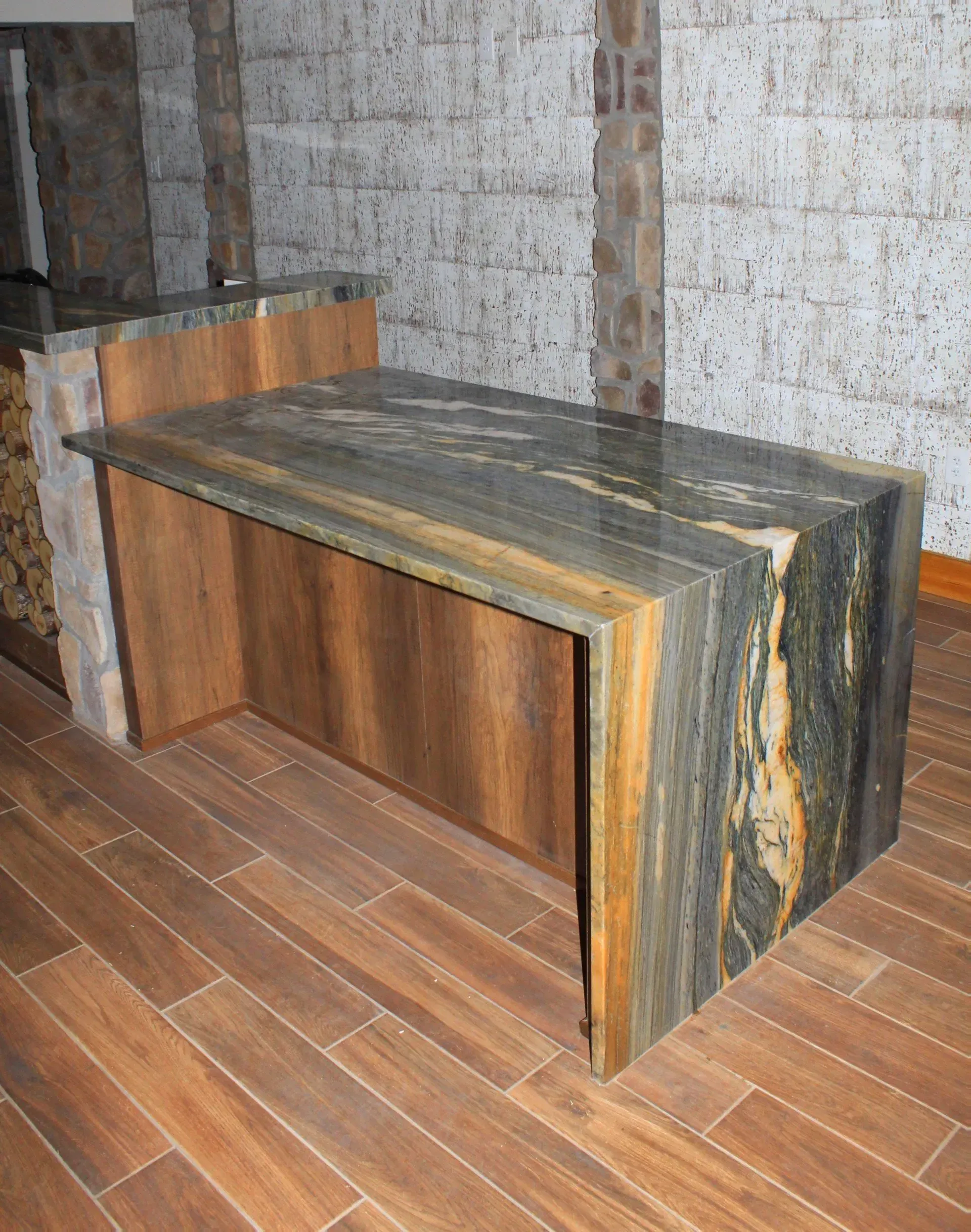 Kitchen island with black, gold, and green granite countertop and wood cabinets, set on wooden floor.