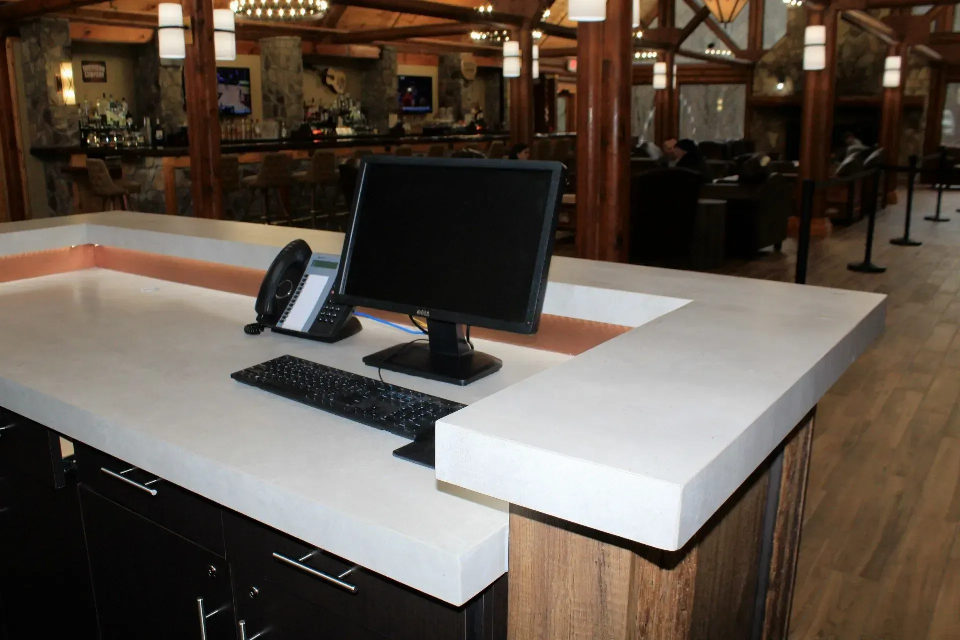 Reception desk with computer, phone, and keyboard in a restaurant with stone and wood interior.