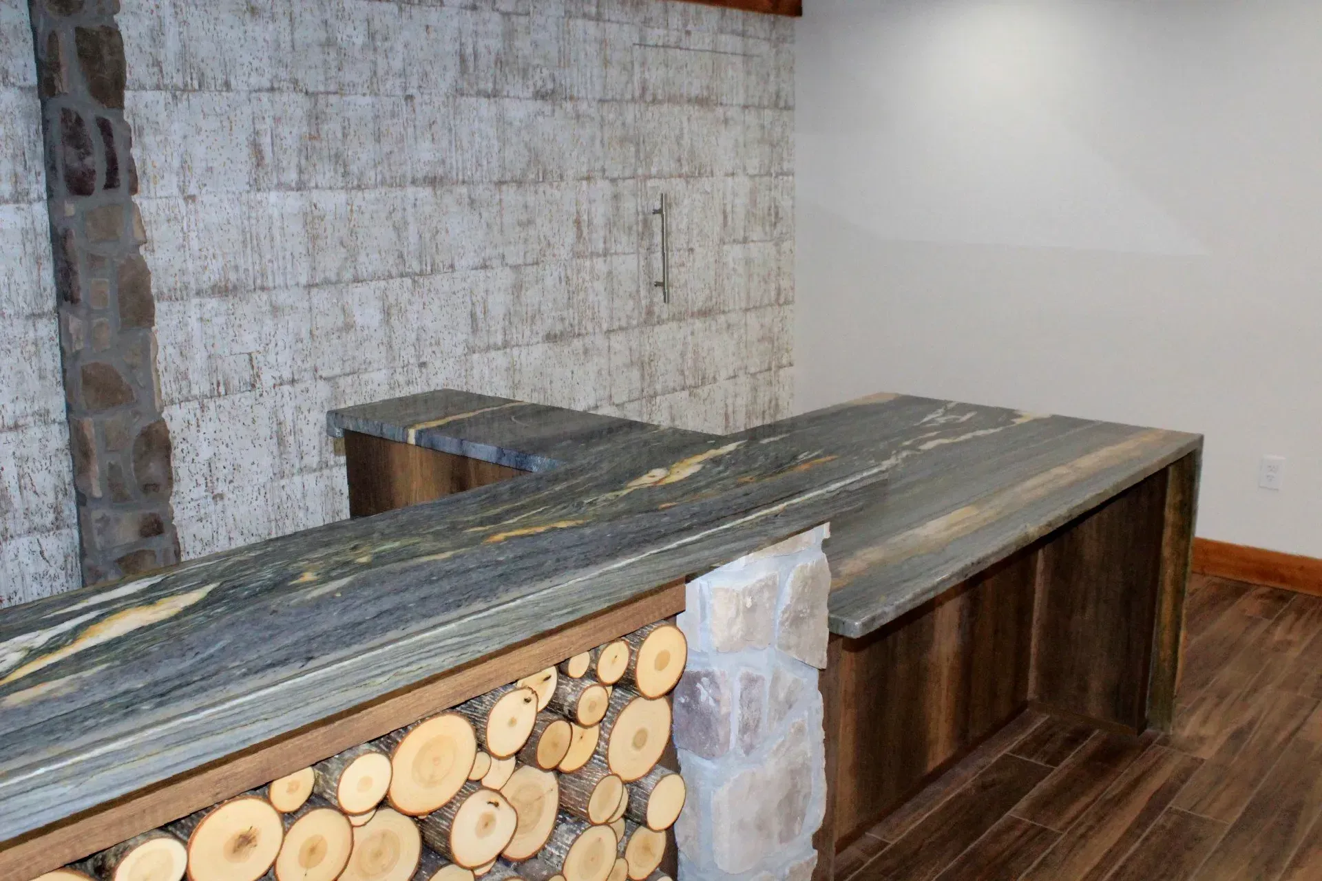 Bar with granite countertop, wood and stacked firewood details, stone accents, and wood flooring.