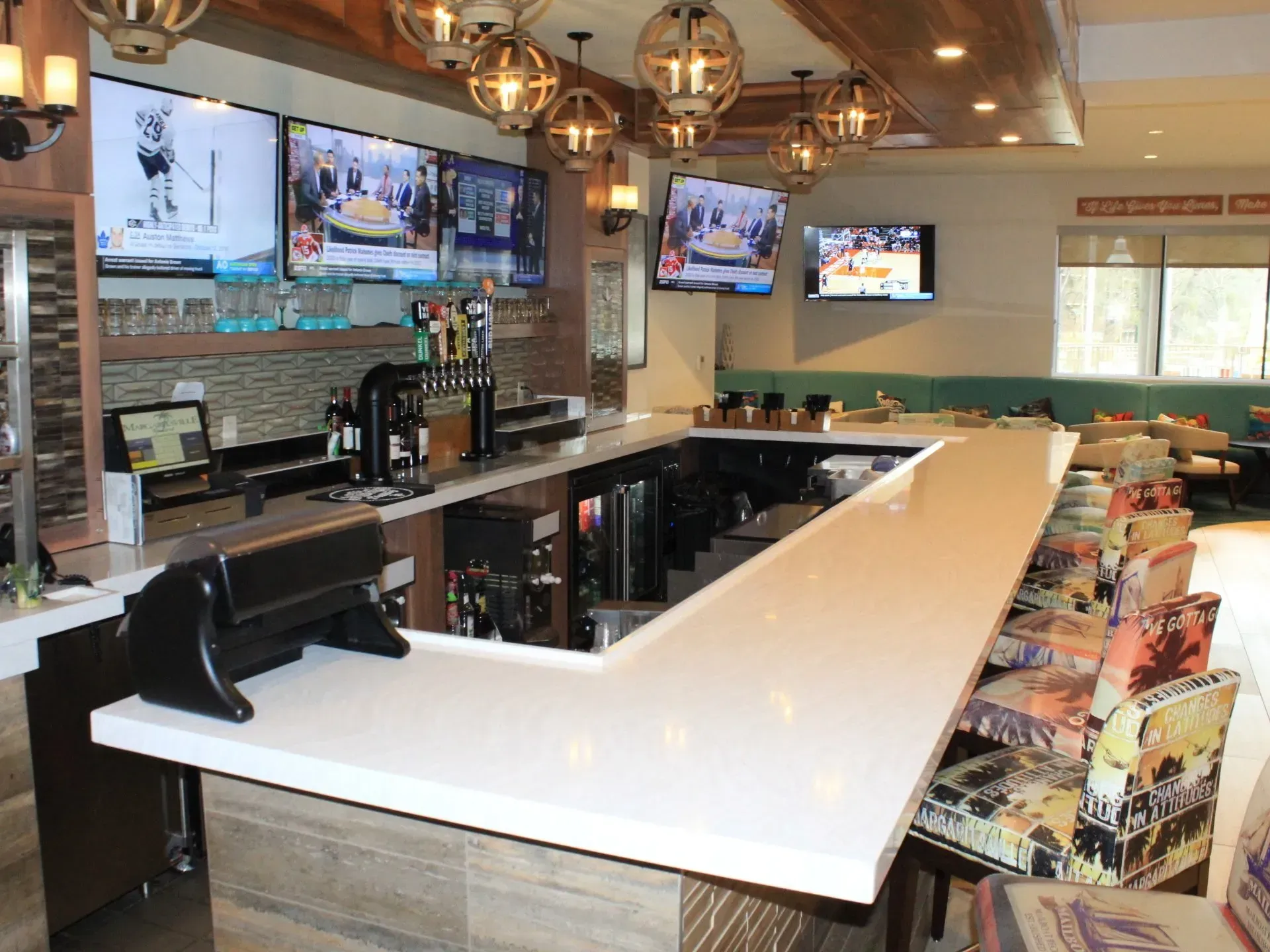 Bar with multiple TVs, draft taps, and seating. Bright white countertop, wood and stone accents.