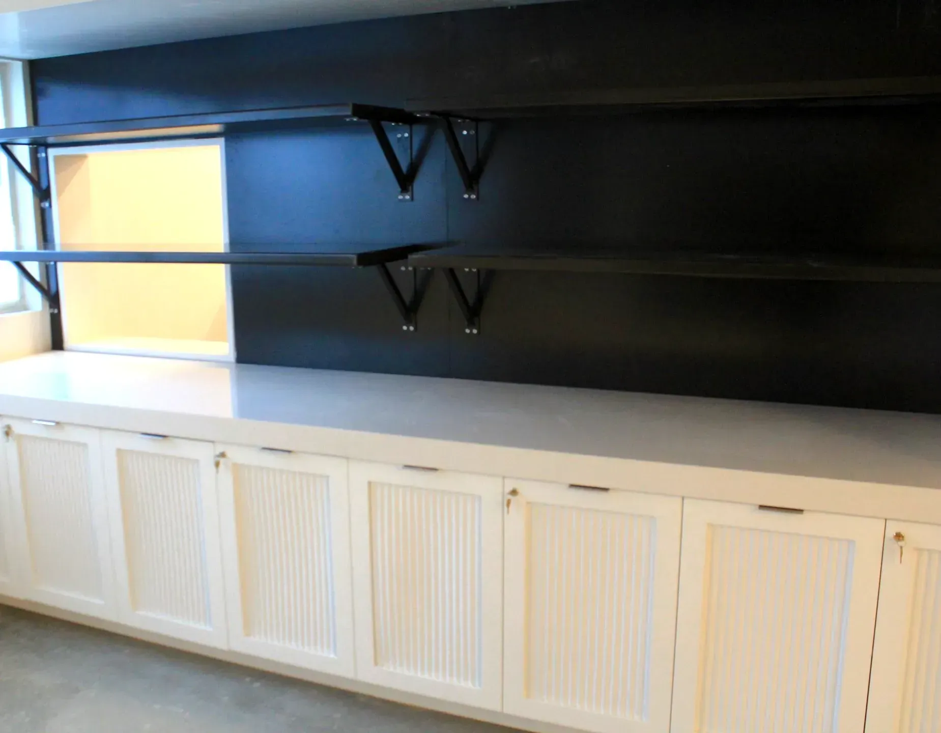 White cabinets below black shelves on a black wall, with a light countertop.