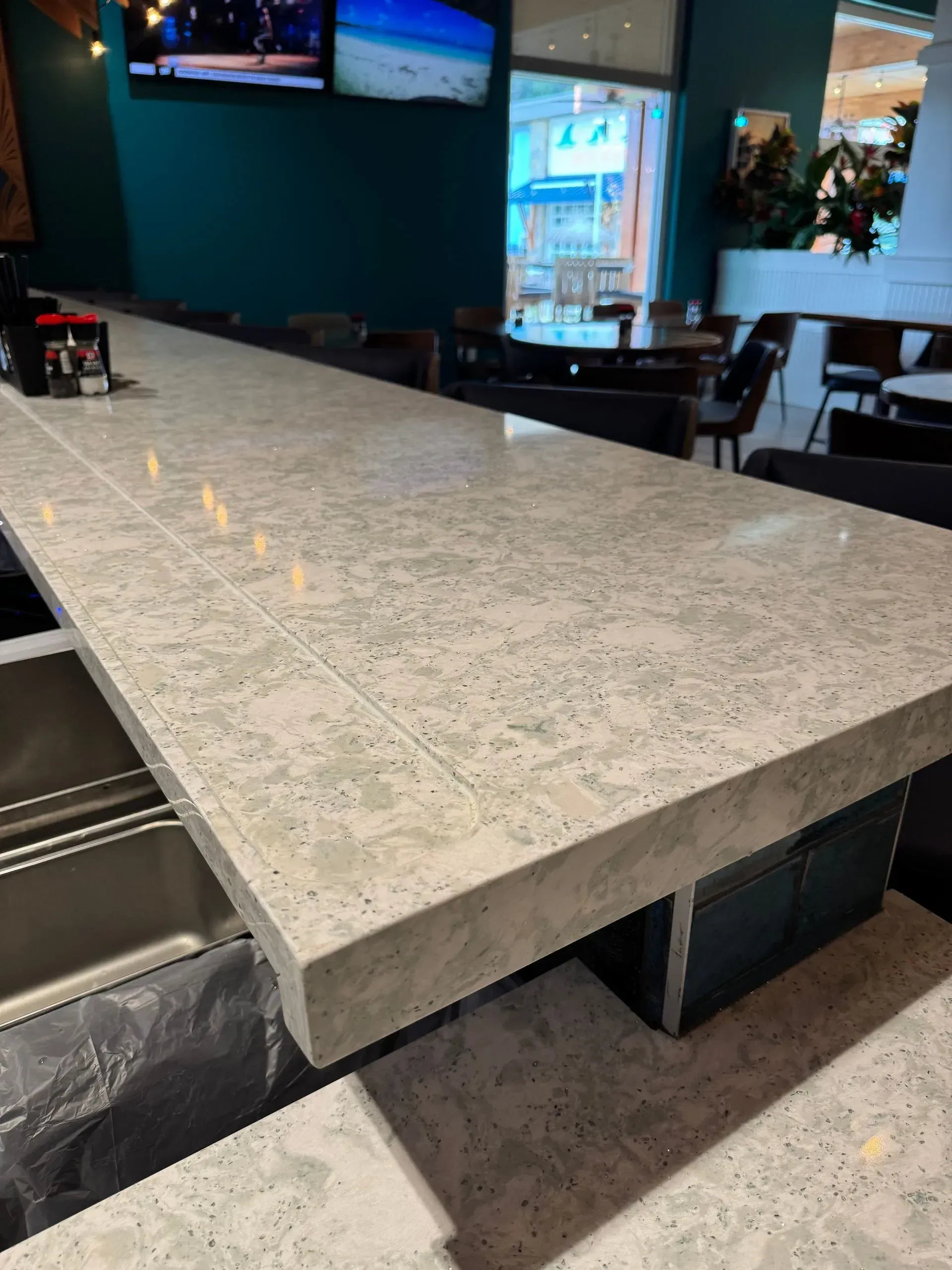 Gray speckled concrete bar in a restaurant, with black support structure and barstools.