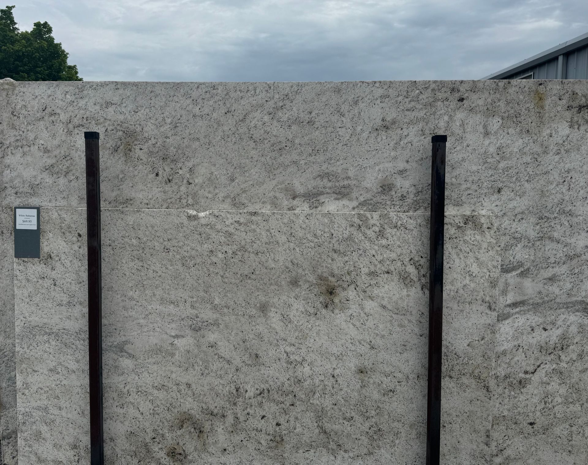 Large white granite slab with dark brown metal supports against a cloudy sky.