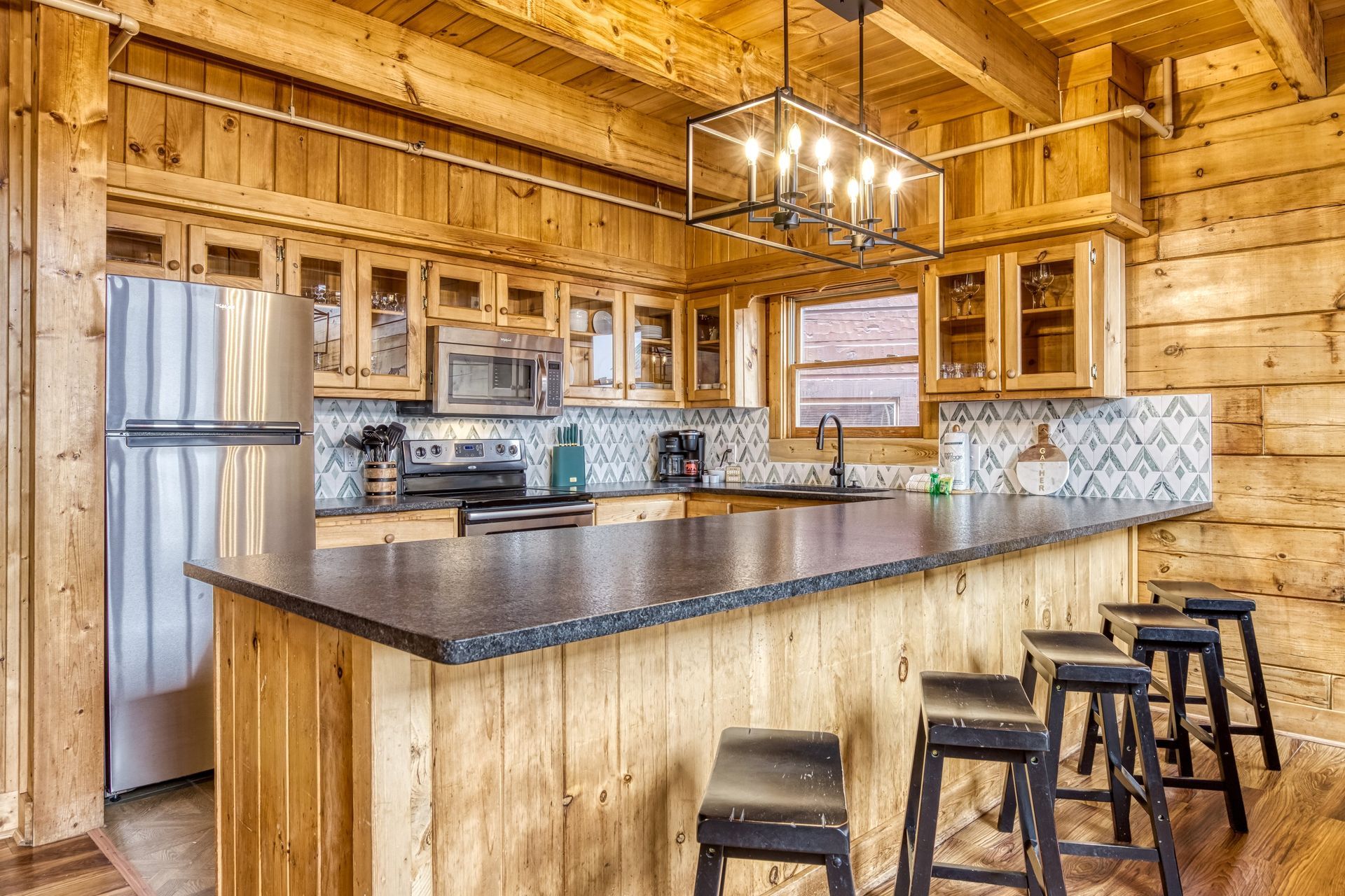 Rustic cabin kitchen with wood cabinets, island, and bar stools. Stainless steel appliances.