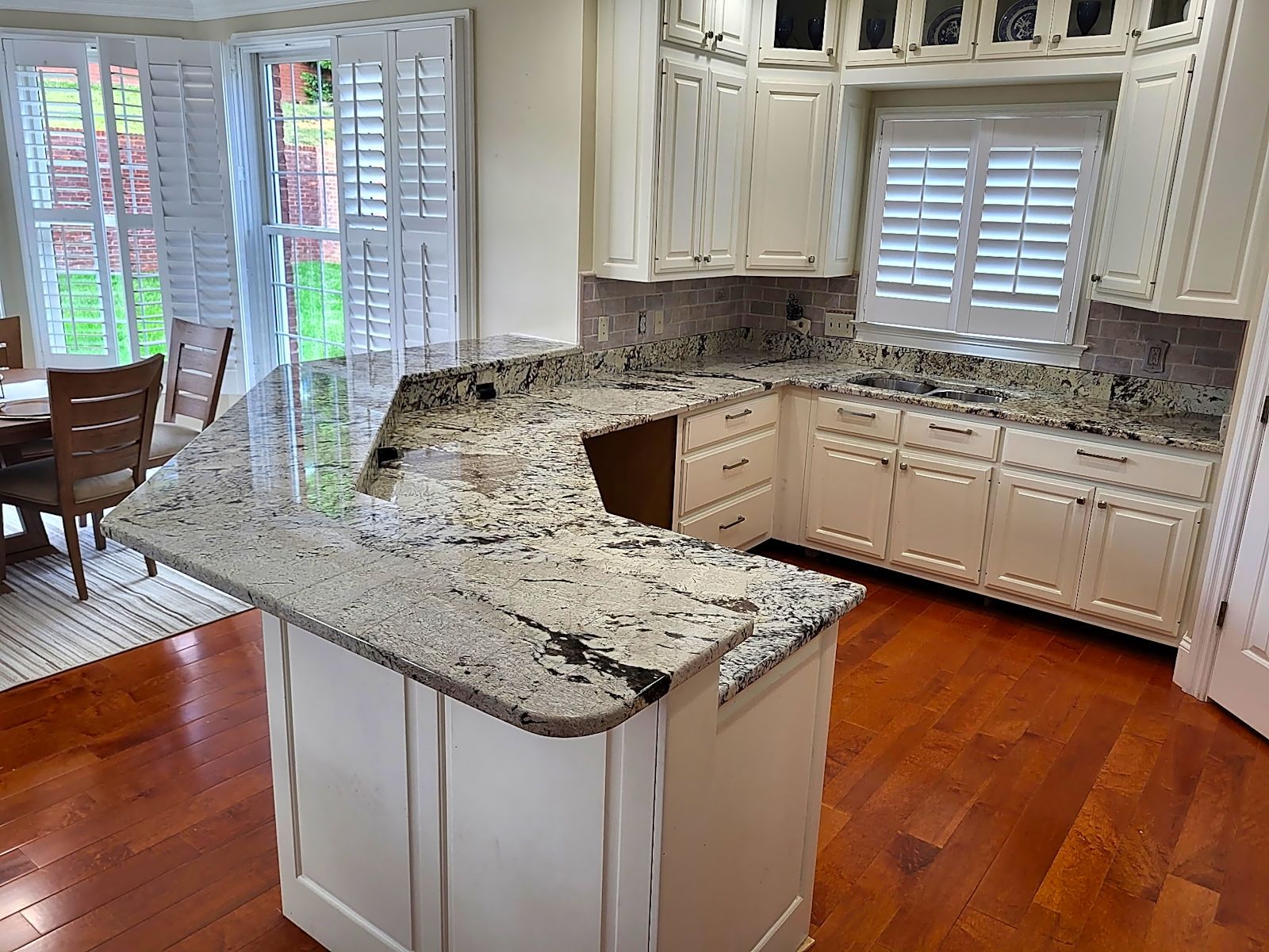 White kitchen with granite countertops, wood floors, and shutters.