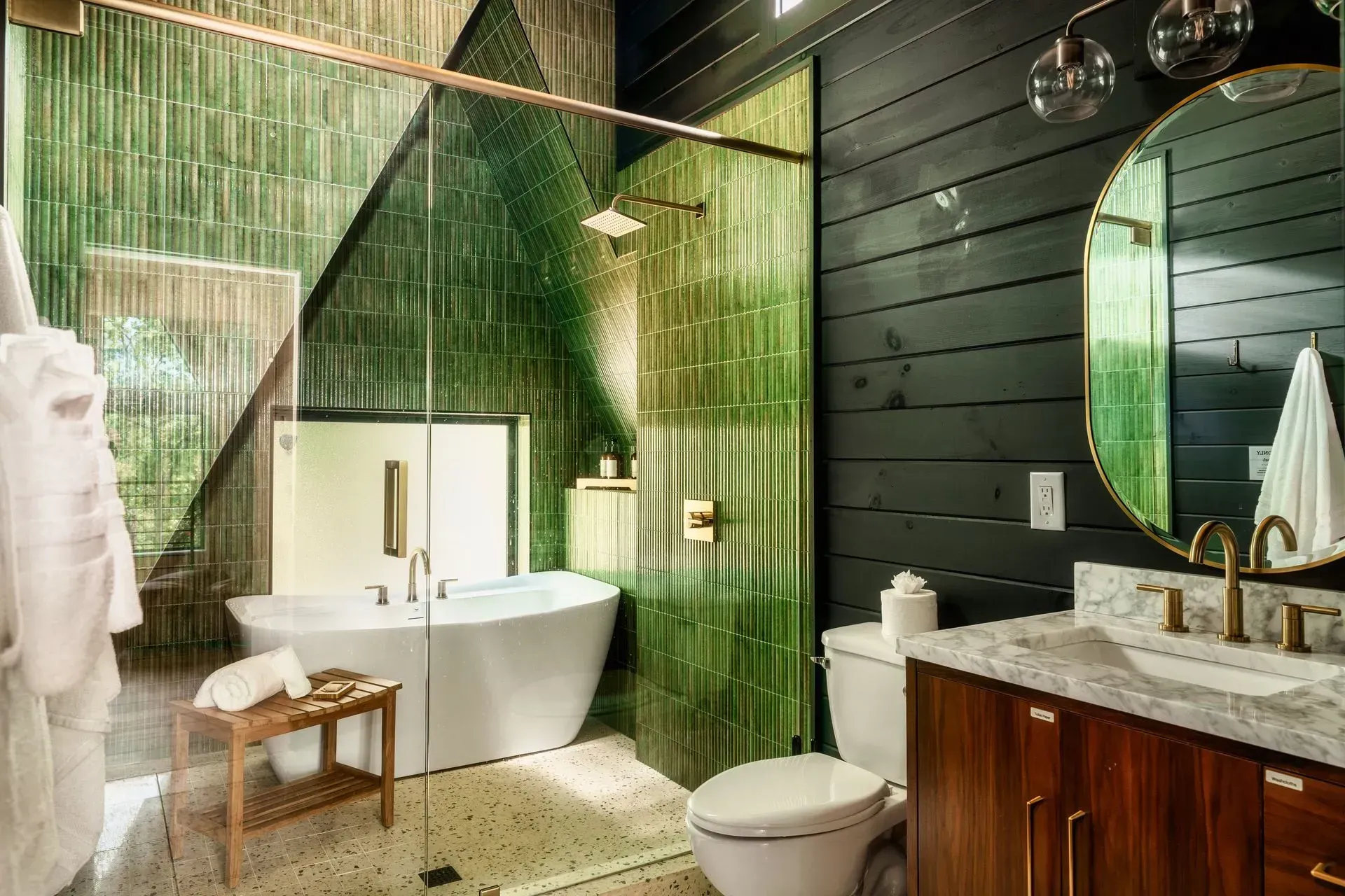 Modern bathroom with green tiled shower, freestanding tub, and marble vanity with round mirror