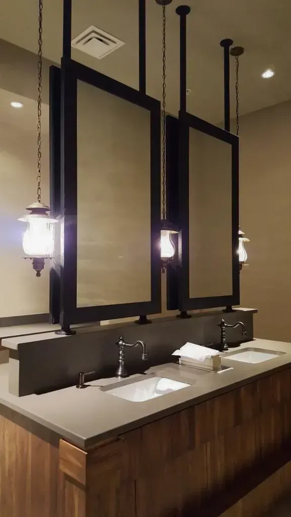 Bathroom with three hanging mirrors, sinks, and pendant lights. Brown and gray tones.