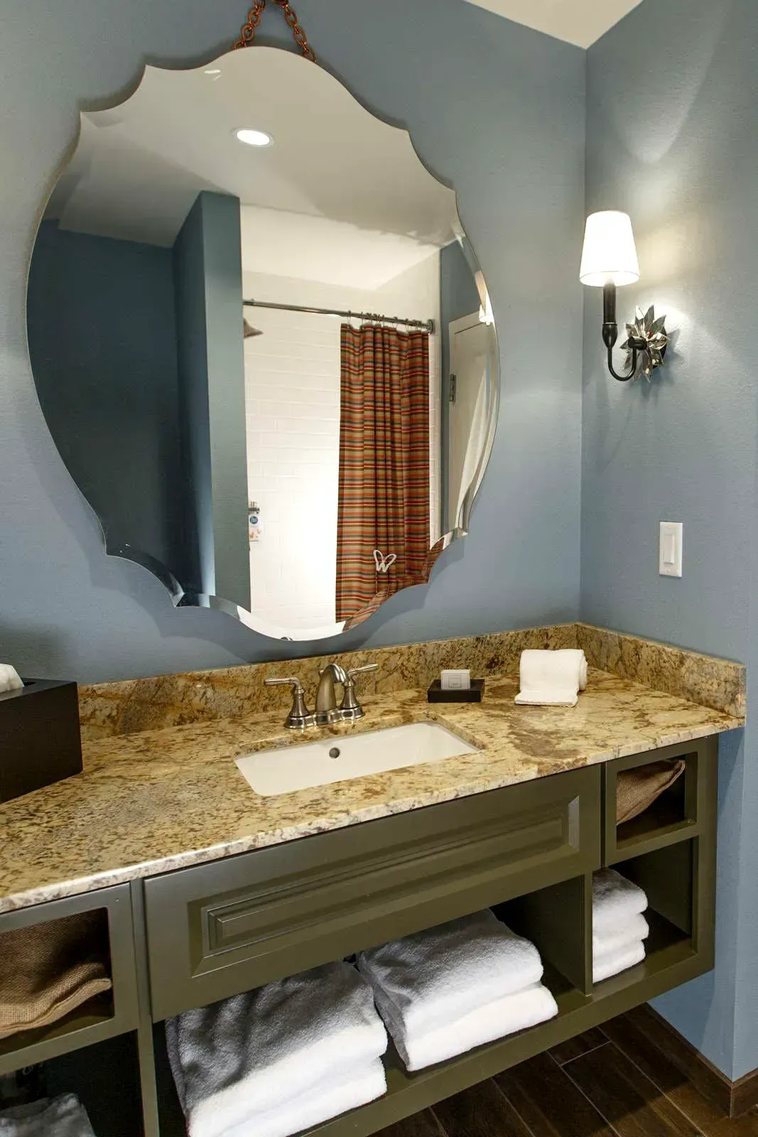 Bathroom with a large decorative mirror, blue walls, a granite countertop, and open shelving.