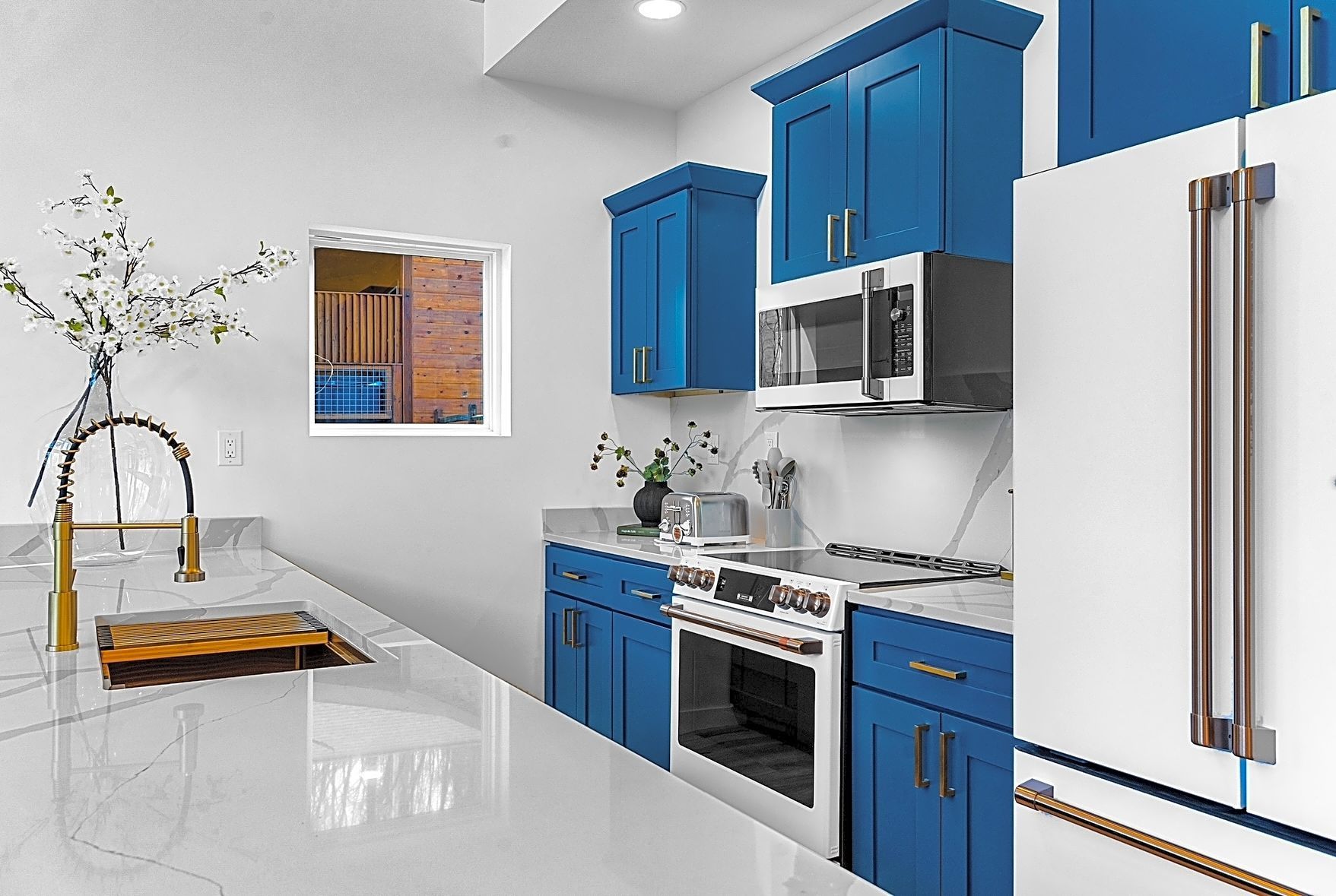 Kitchen with white countertops, blue cabinets, stainless steel appliances, and a window.