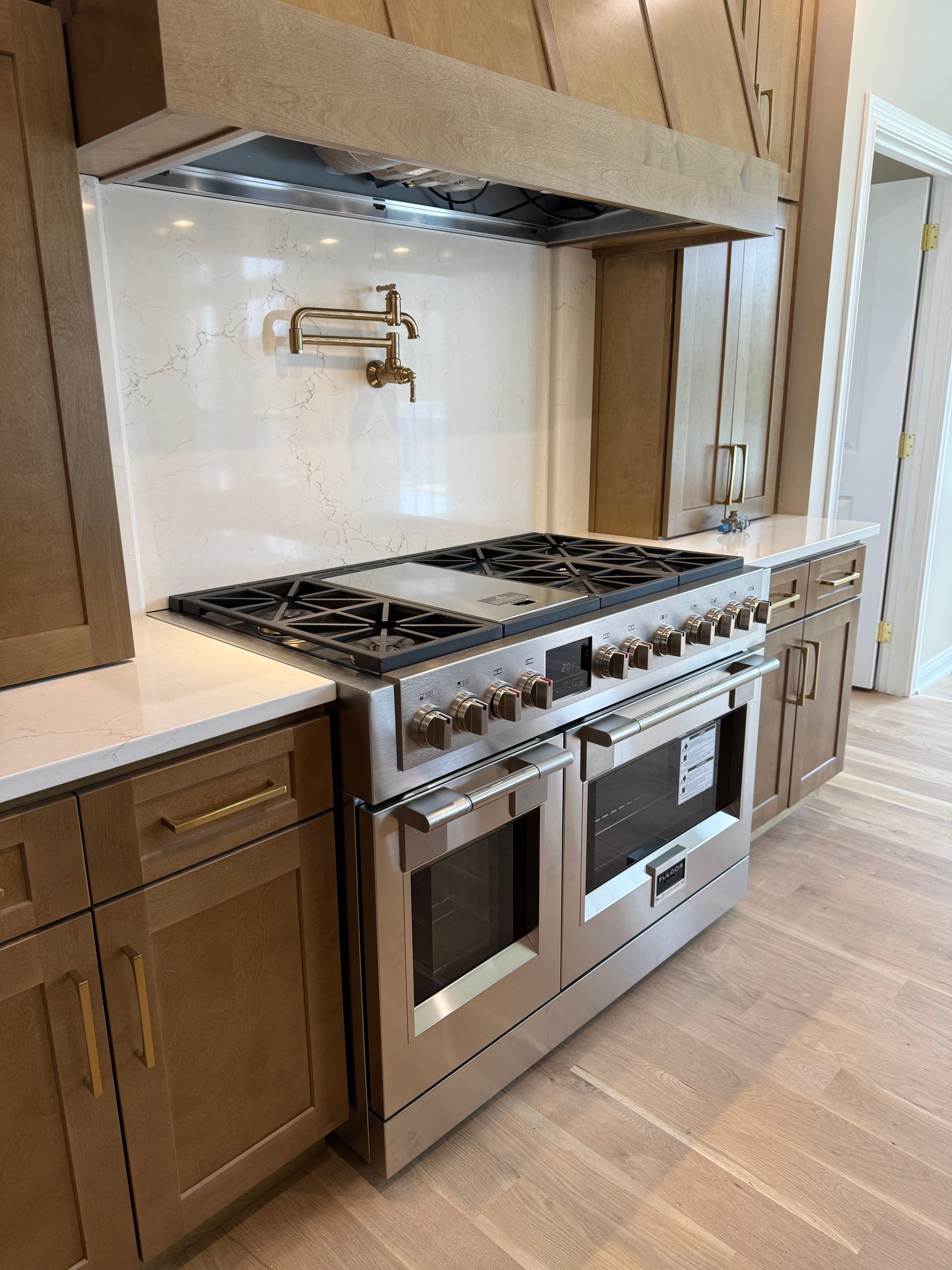 Stainless steel oven and stove in a kitchen with tan cabinets and a light wood floor.
