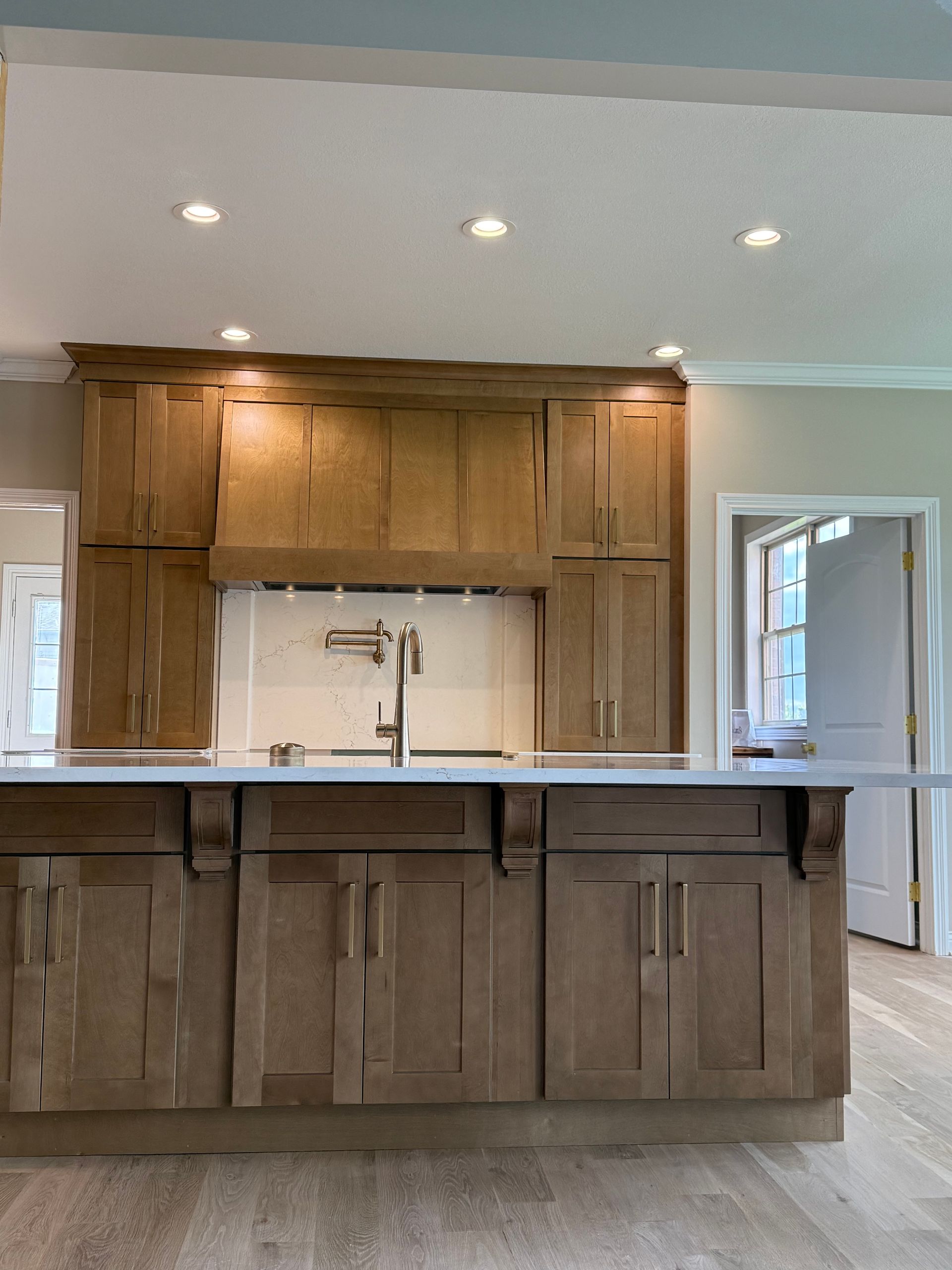 Kitchen with light wood cabinets, countertop, and a faucet; recessed lighting.