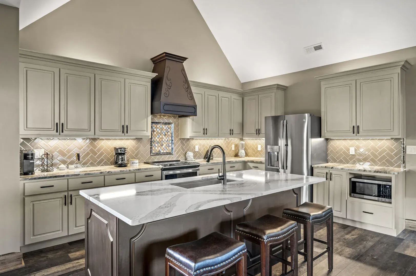 Kitchen with light green cabinets, marble countertops, stainless steel appliances, and a dark brown island.