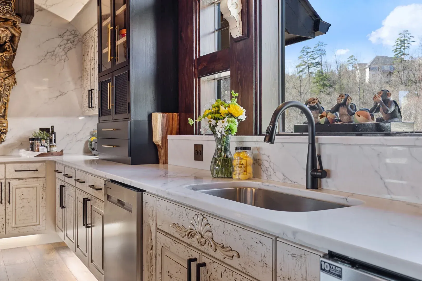 Modern kitchen with marble countertops, stainless steel sink, black faucet, and view of trees.