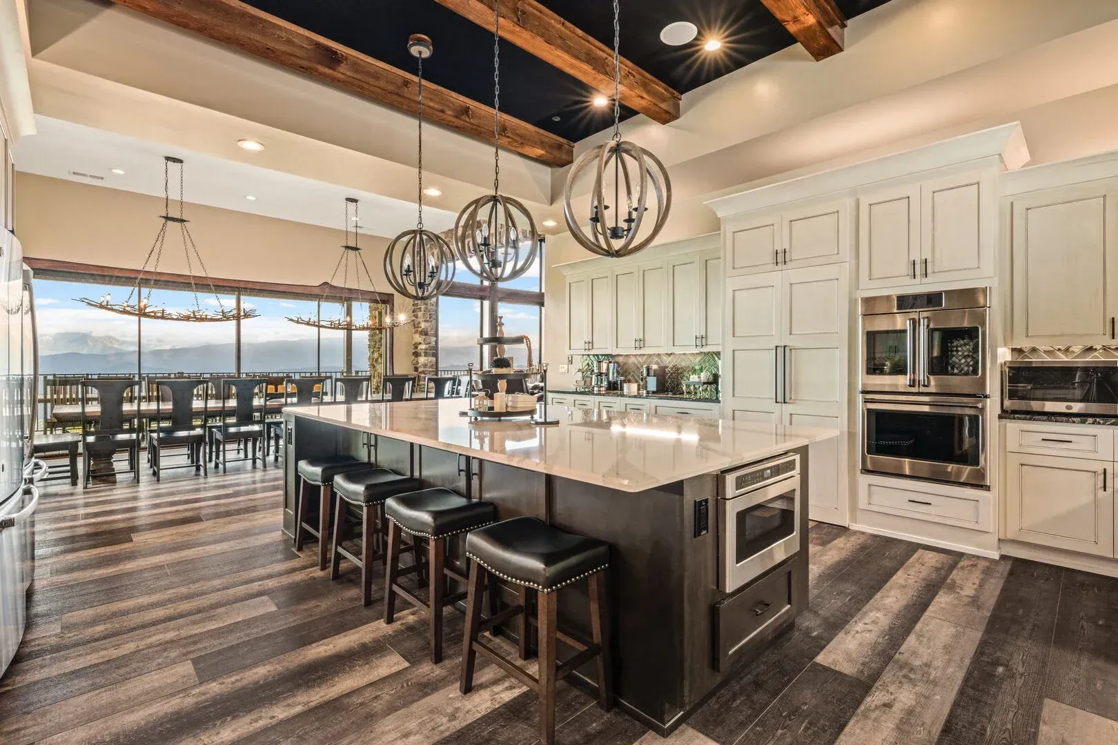 Modern kitchen with large island, white cabinets, dark wood floors, and chandeliers.