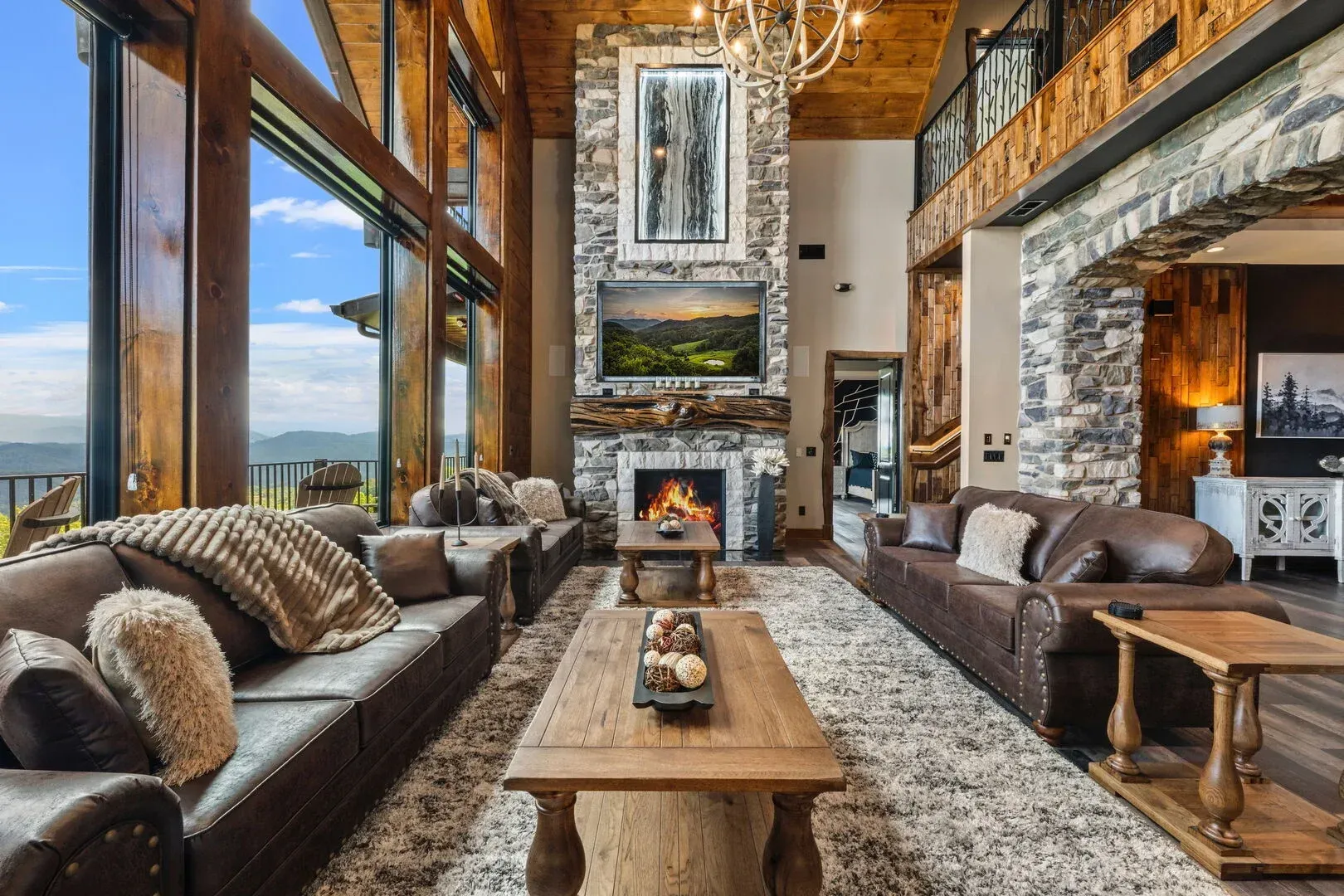 Living room with large windows, fireplace, and leather couches, in a mountain home.