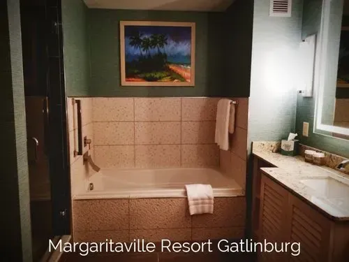 Bathroom at Margaritaville Resort Gatlinburg, with a tub, shower, and vanity. Green walls, beach painting, and beige tiles.